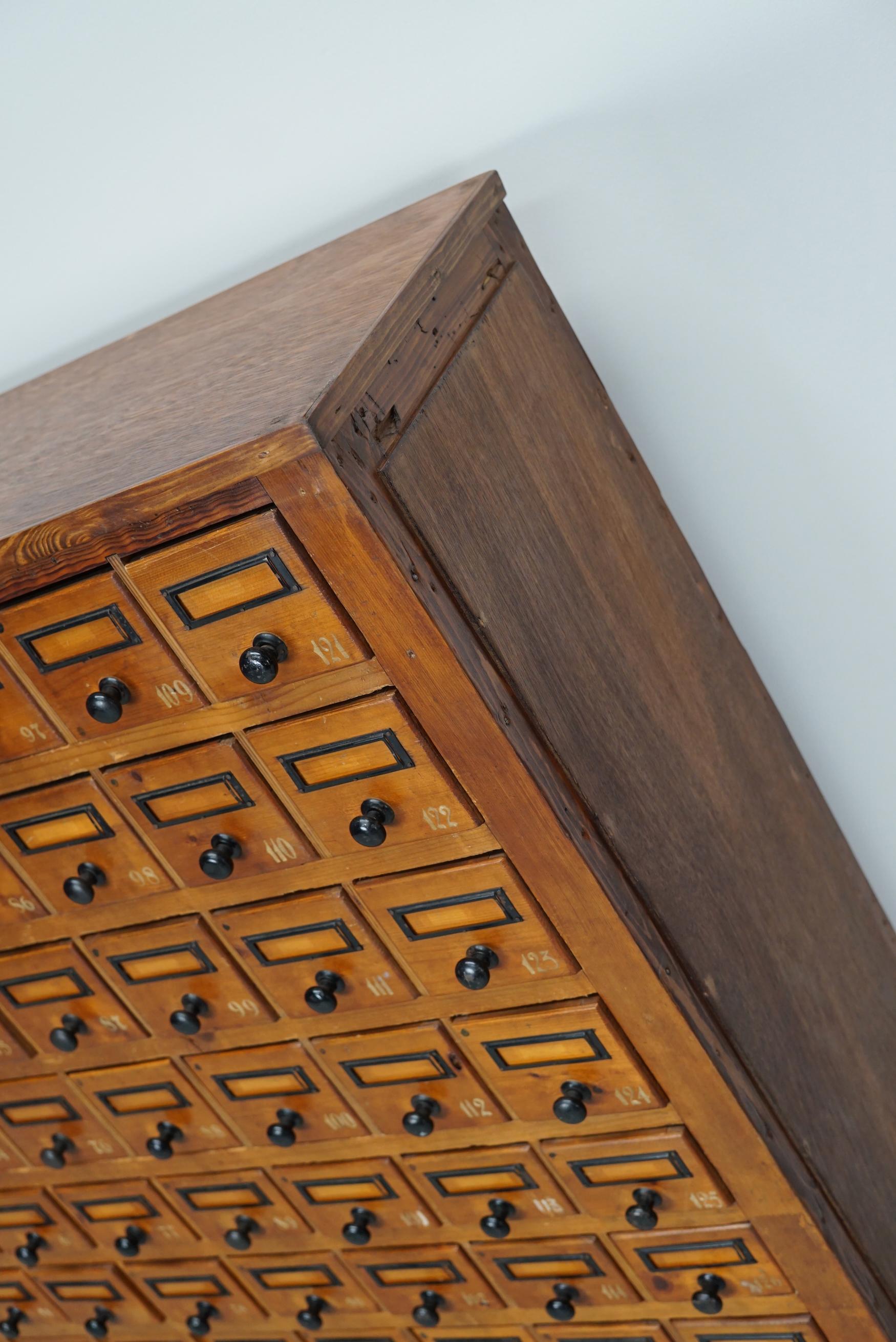 Cette armoire d'atelier a été fabriquée en pin aux Pays-Bas vers les années 1930 et a été utilisée dans un atelier pour l'équipement d'un dentiste. Il comporte de nombreux tiroirs avec de petits boutons et des porte-cartes. Les dimensions