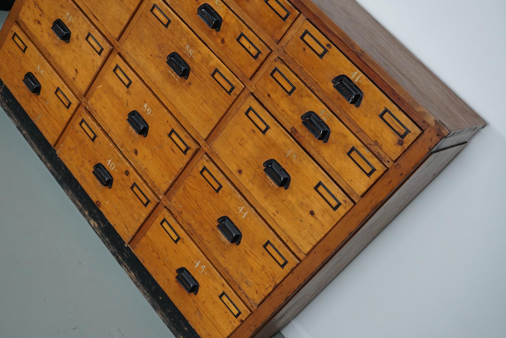 Cette armoire d'atelier a été fabriquée en pin aux Pays-Bas vers les années 1930 et a été utilisée dans un atelier pour l'équipement d'un dentiste. Il comporte de nombreux tiroirs avec de jolies poignées et des porte-cartes. Les dimensions
