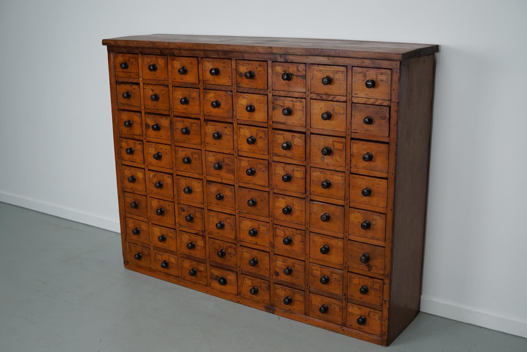 Este armario de taller se fabricó en pino en Holanda hacia la década de 1930 y se utilizaba en un taller para equipos de dentista. Tiene muchos cajones con pomos negros. Las dimensiones interiores de los cajones son DAP 29 x 13 x 10 cm. El mueble ha