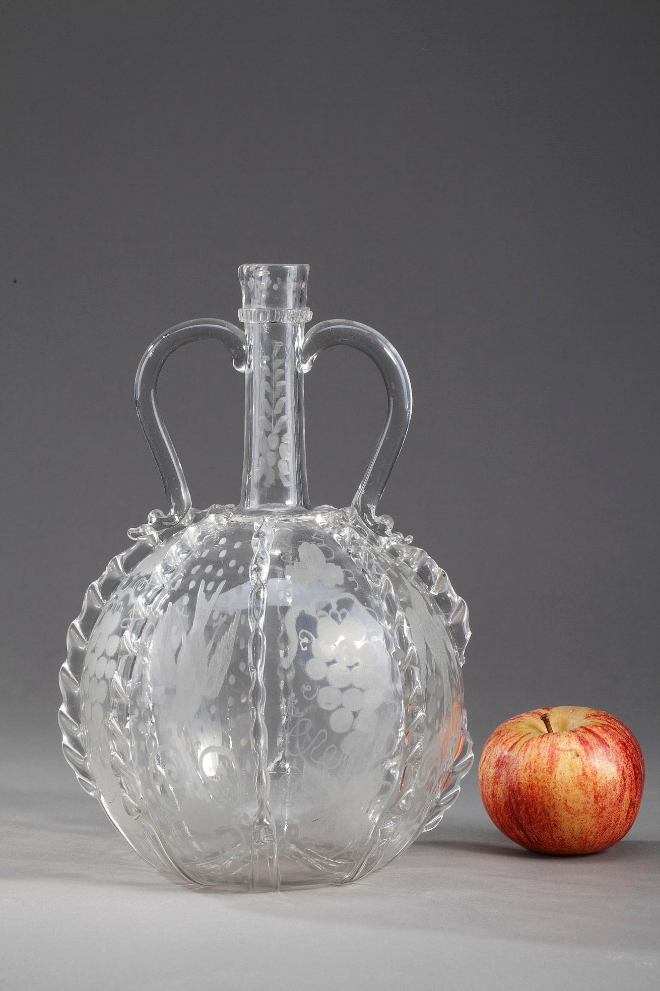 Glass Dutch jug with long neck and two handles. It is decorated with glass ribbons worked with pliers
and with grape and bird motifs. It is made of blown glass, stretched and engraved with sand. It is a
typical work of the late eighteenth - early