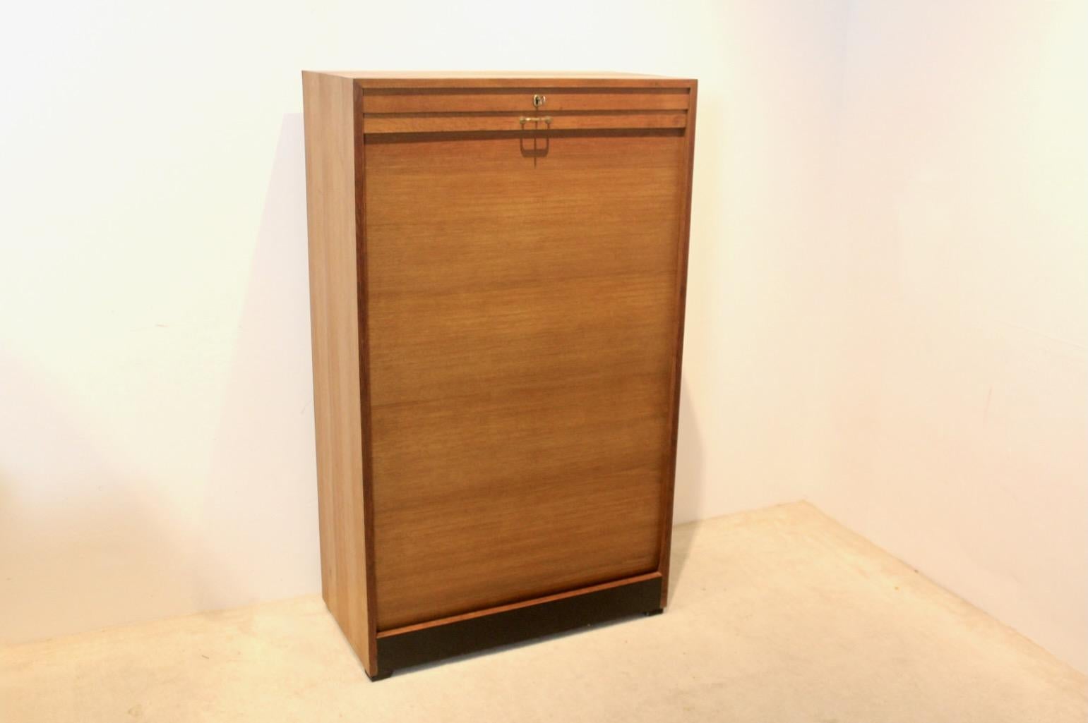 Elegante mueble biblioteca holandés de los años 60 en chapa de roble con una sofisticada puerta corredera. Con 18 casilleros superiores sobre un armario con estantes inferior. Cerradura de trabajo con llave. Restos de una antigua biblioteca de
