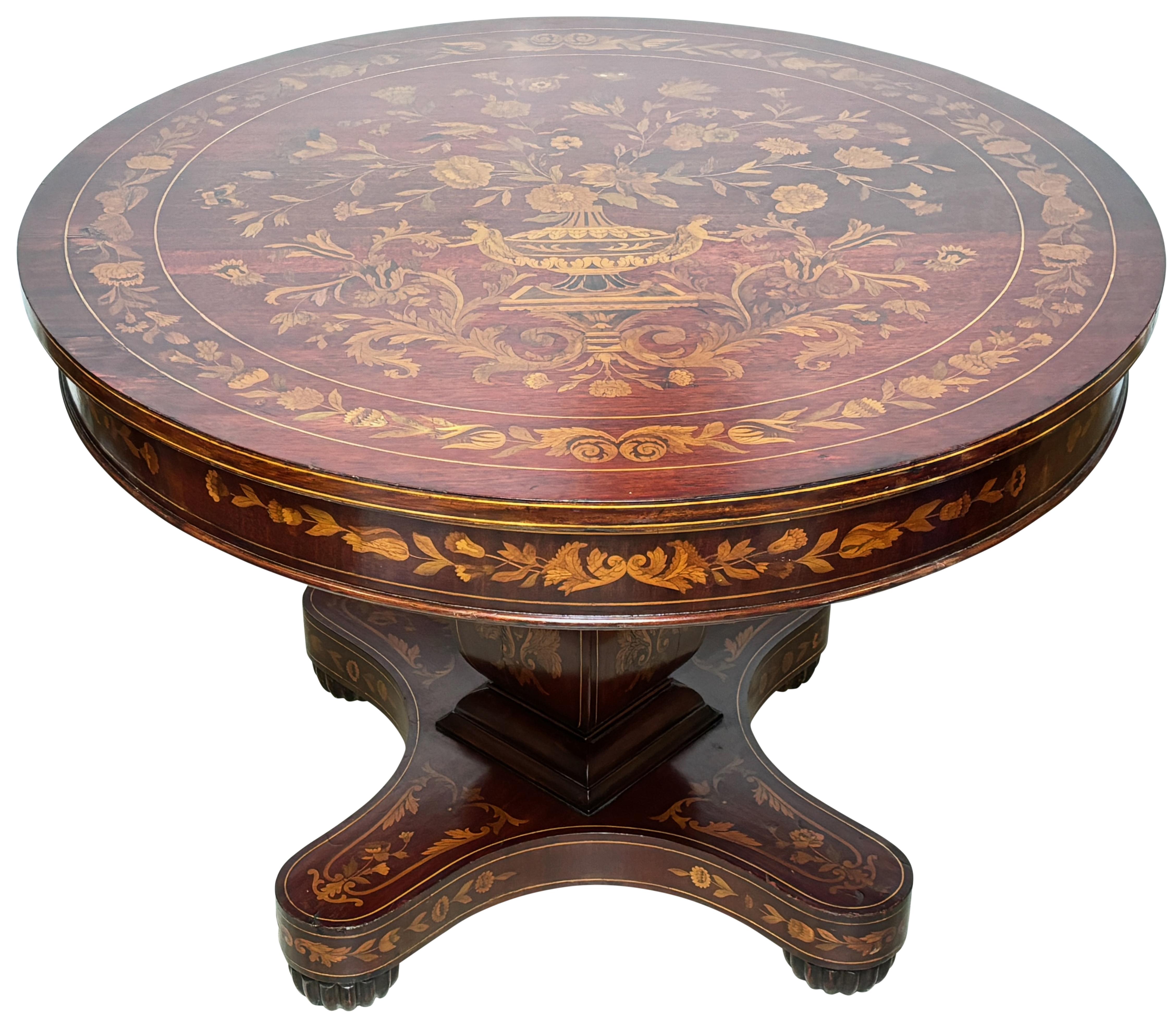 Cette exquise table centrale en acajou et marqueterie de bois fruitier offre une présence sophistiquée à toute maison haut de gamme. Le plateau circulaire est surmonté d'une frise marquetée conforme, avec un motif global de marqueterie de bois