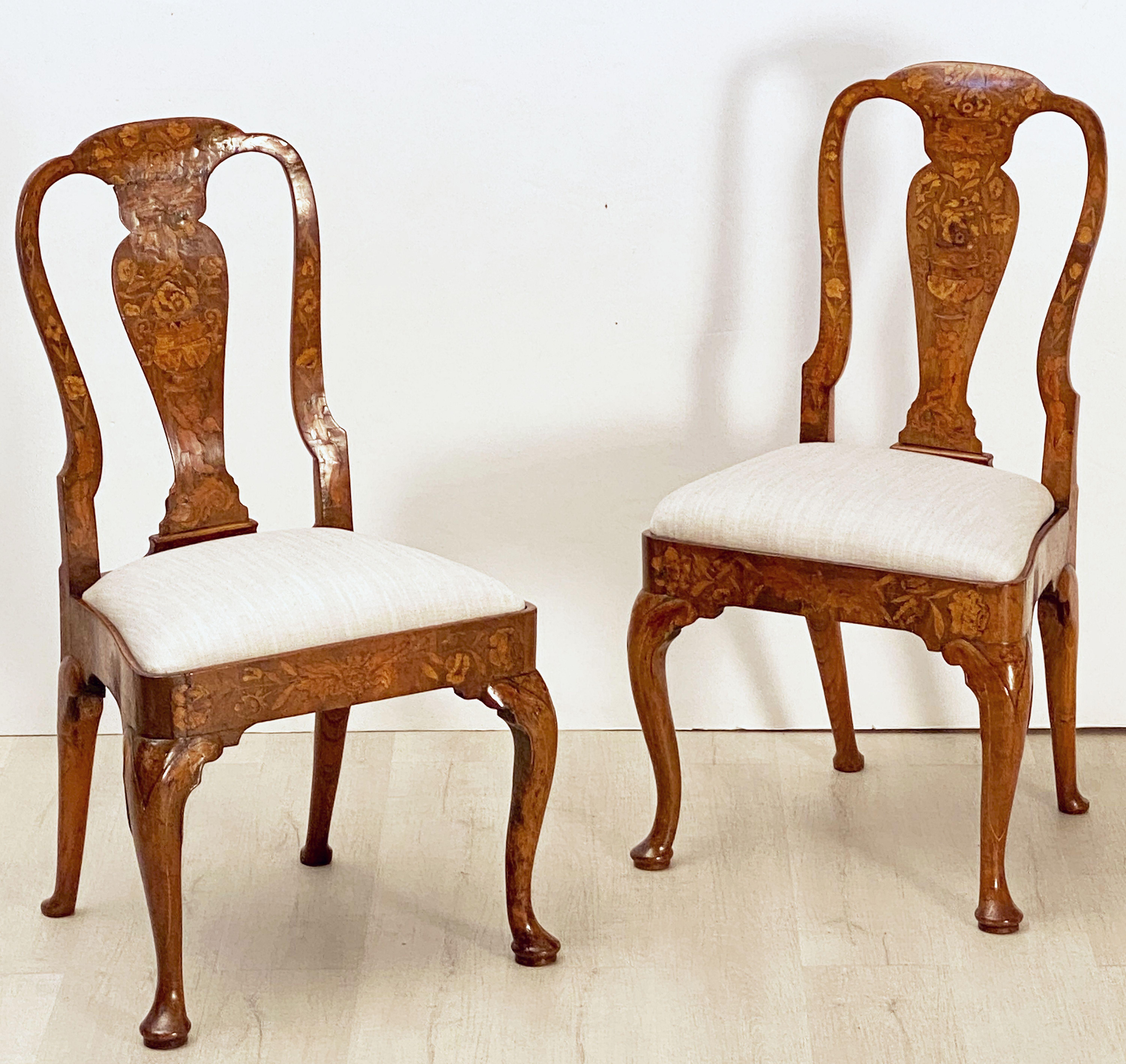 A very fine pair of Dutch marquetry chairs of elm and walnut from the early 19th century - each chair featuring an inlaid design of a cherub holding up a vase and urn with flowers to the back, over a frame with upholstered seat and resting on