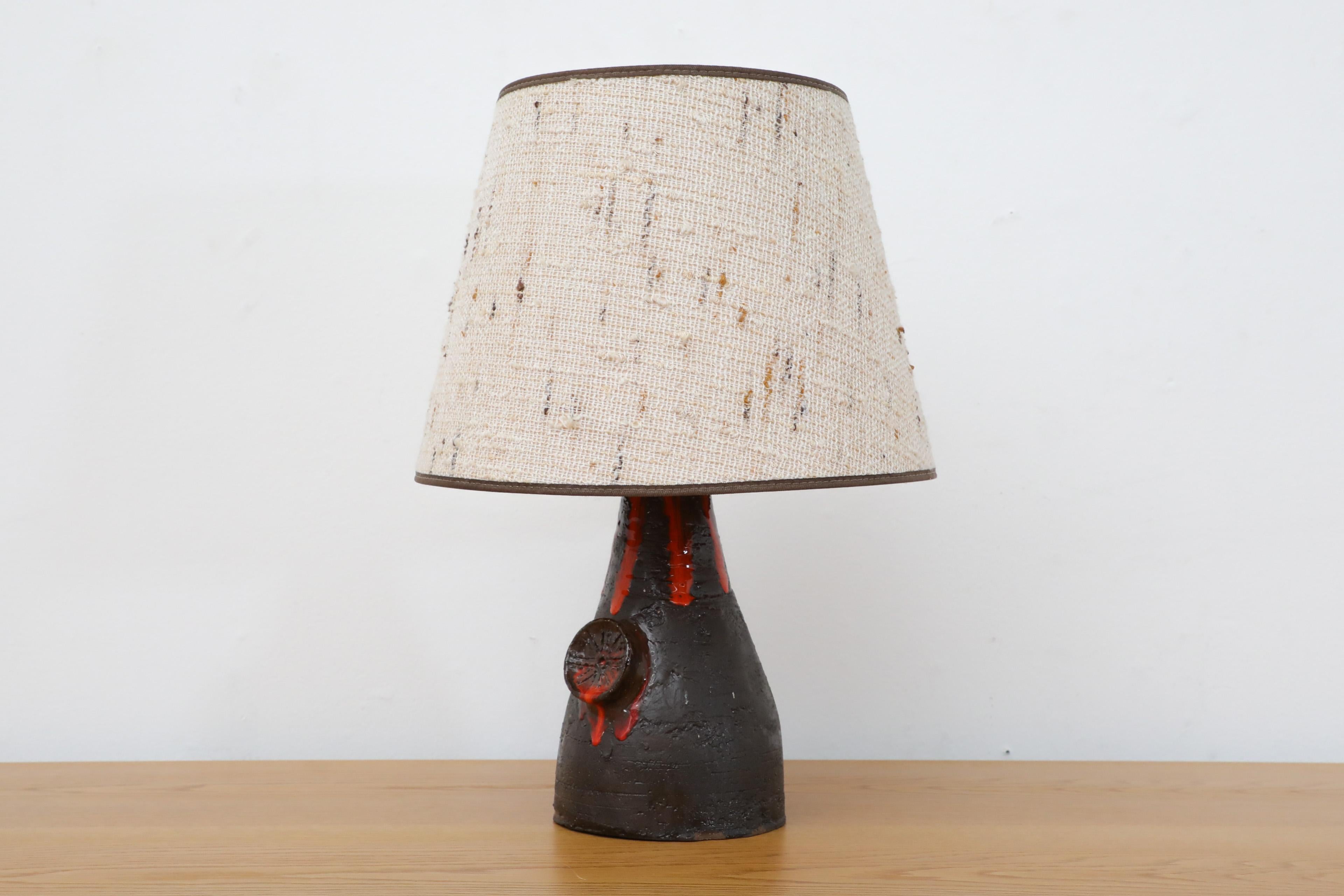 Dutch Mid-Century black glazed ceramic table lamp with volcanic impression and dripping fire-like red glaze. The shade is a fabric tapered drum. In original condition with wear consistent with age and use.