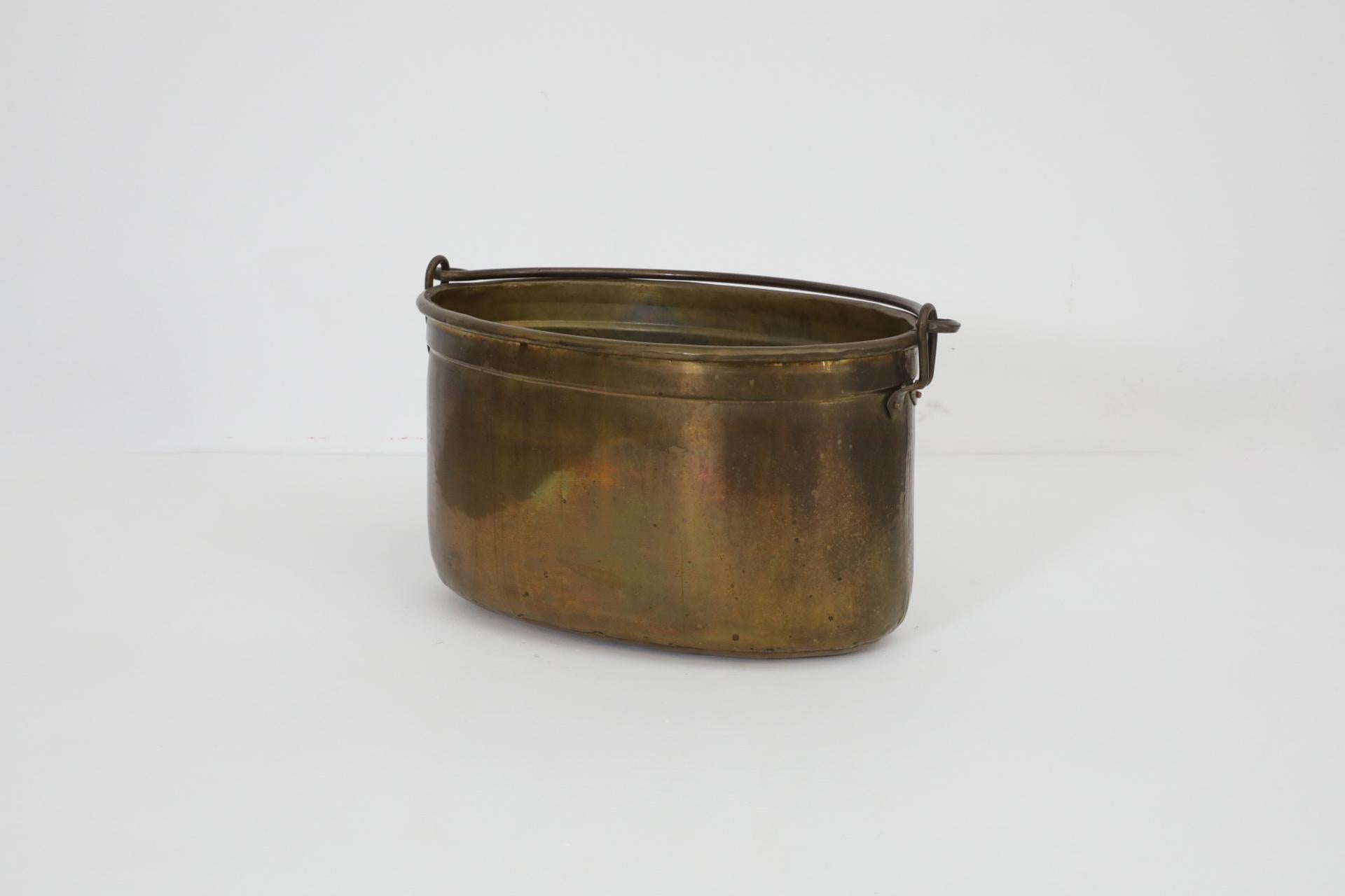 Dutch Mid-Century, 1950's/60's, oval shaped and handsomely made brass bucket with a decorative handle. Its original use was storing or carrying firewood for a fireplace. All original condition with visible wear and lovely, deep patina. Wear is