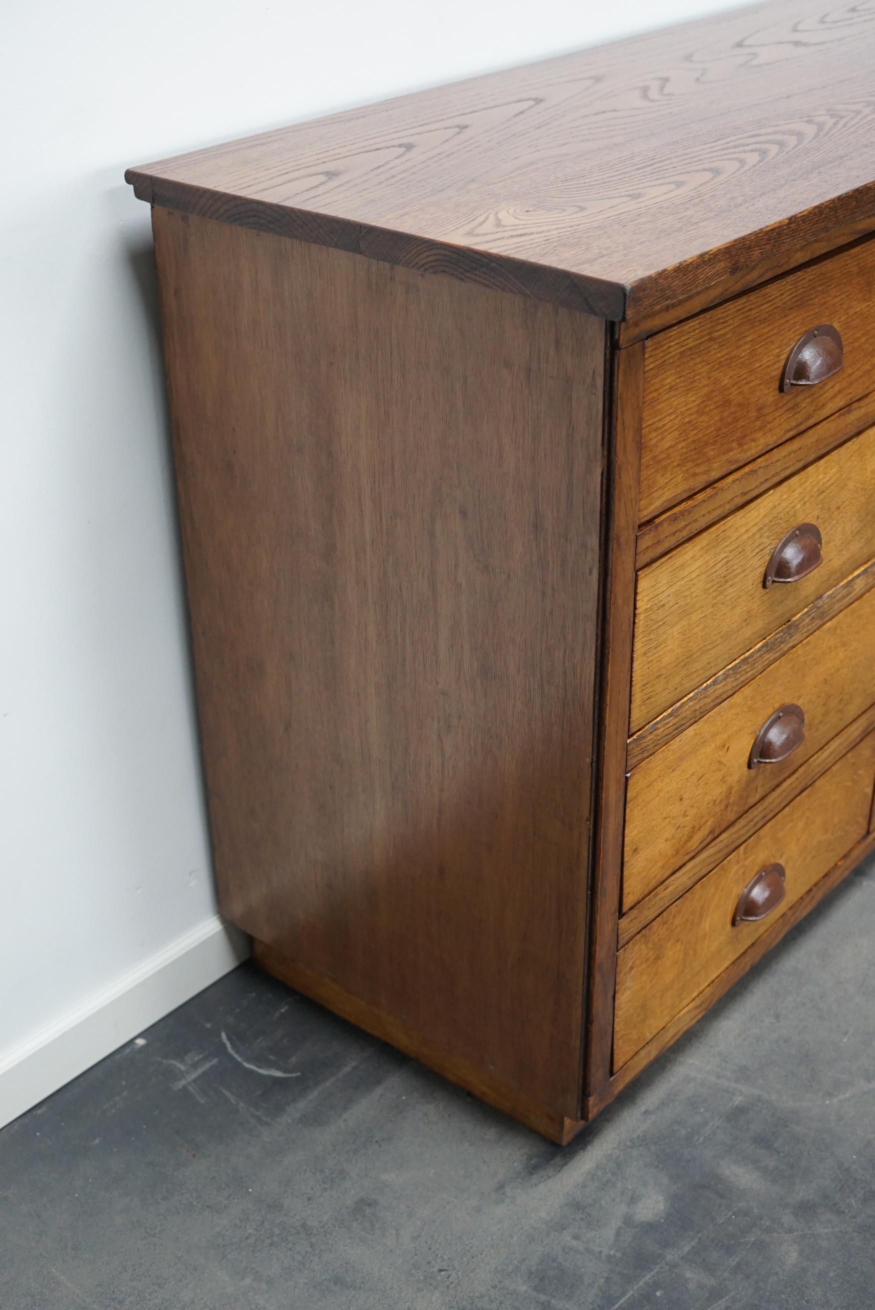 This apothecary cabinet was designed and made from oak circa 1950 in the Netherlands. It features 12 decent sized drawers with metal hardware. The inside of the drawers measure: DWH 37 x 42 x 12 cm.