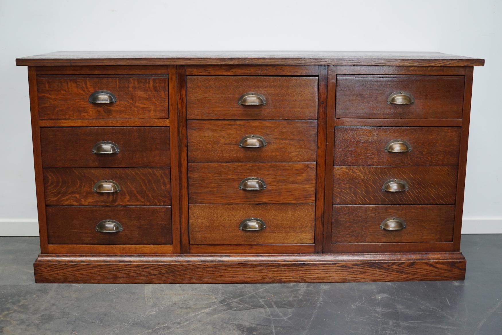 This apothecary cabinet was designed and made from oak circa 1930 in the Netherlands. It features 12 decent sized drawers with brass hardware. The inside of the drawers measure: DWH 41 x 38 x 11 cm.