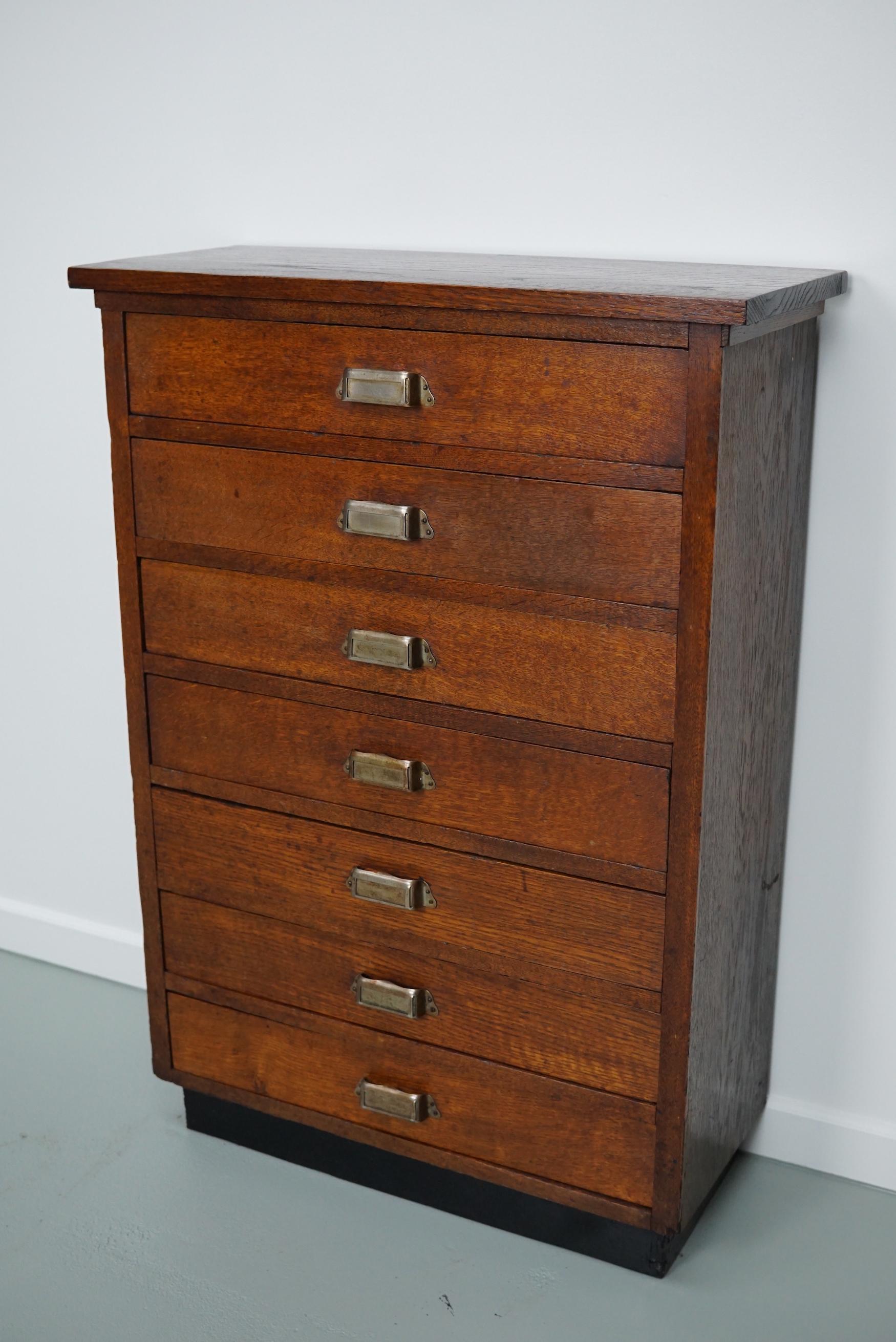 This apothecary cabinet was designed and made from oak circa 1930 in the Netherlands. It features 7 drawers with brass hardware. The inside of the drawers measure: DWH 18 x 52 x 8 cm.