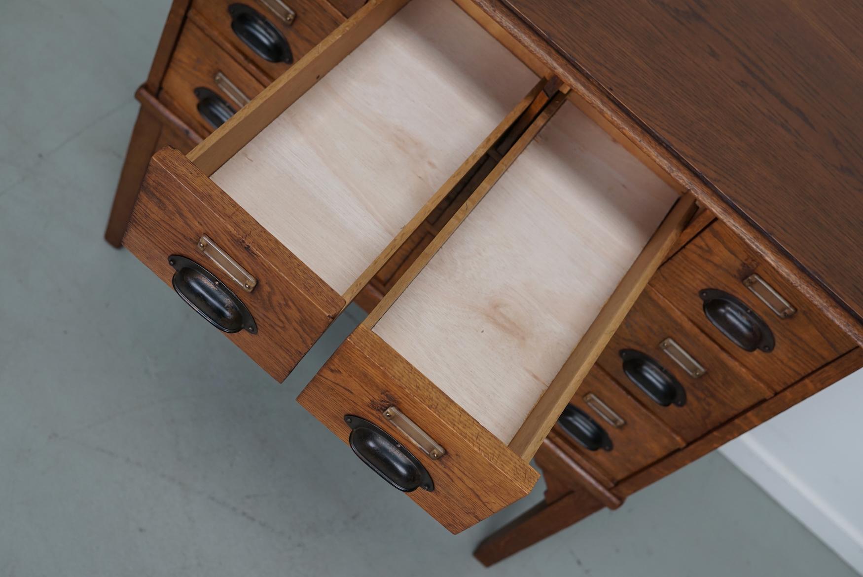 This apothecary cabinet was designed and made from oak and veneer circa 1930 in the Netherlands. It features 12 drawers with black metal hardware. The inside of the drawers measure: DWH 44 x 16 x 7 / 13 cm. 