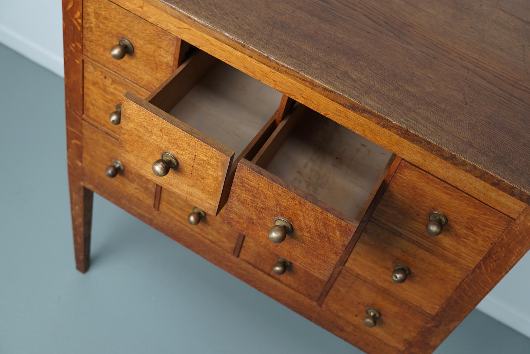 This apothecary cabinet was designed and made from oak circa 1930 in the Netherlands. It features 12 drawers with brass hardware. The inside of the drawers measure: DWH 47 x 16 / 8 x 13 cm.