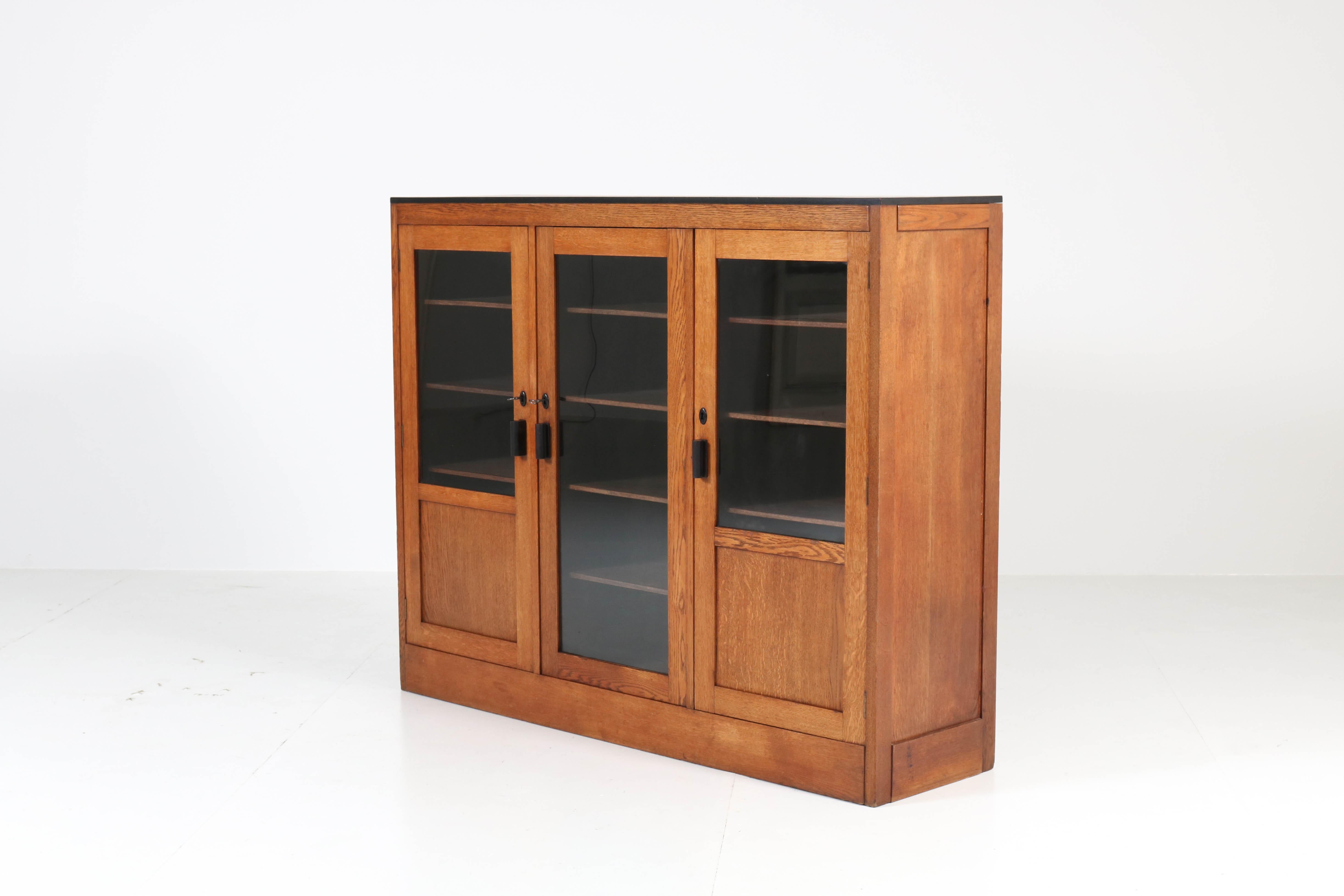 Wonderful Art Deco Haagse School bookcase.
Design by Gescher & Kemper Amsterdam.
Marked with metal tag.
Striking Dutch design from the twenties.
Oak with original ebonized top and handles.
12 original wooden shelves adjustable in height.
In
