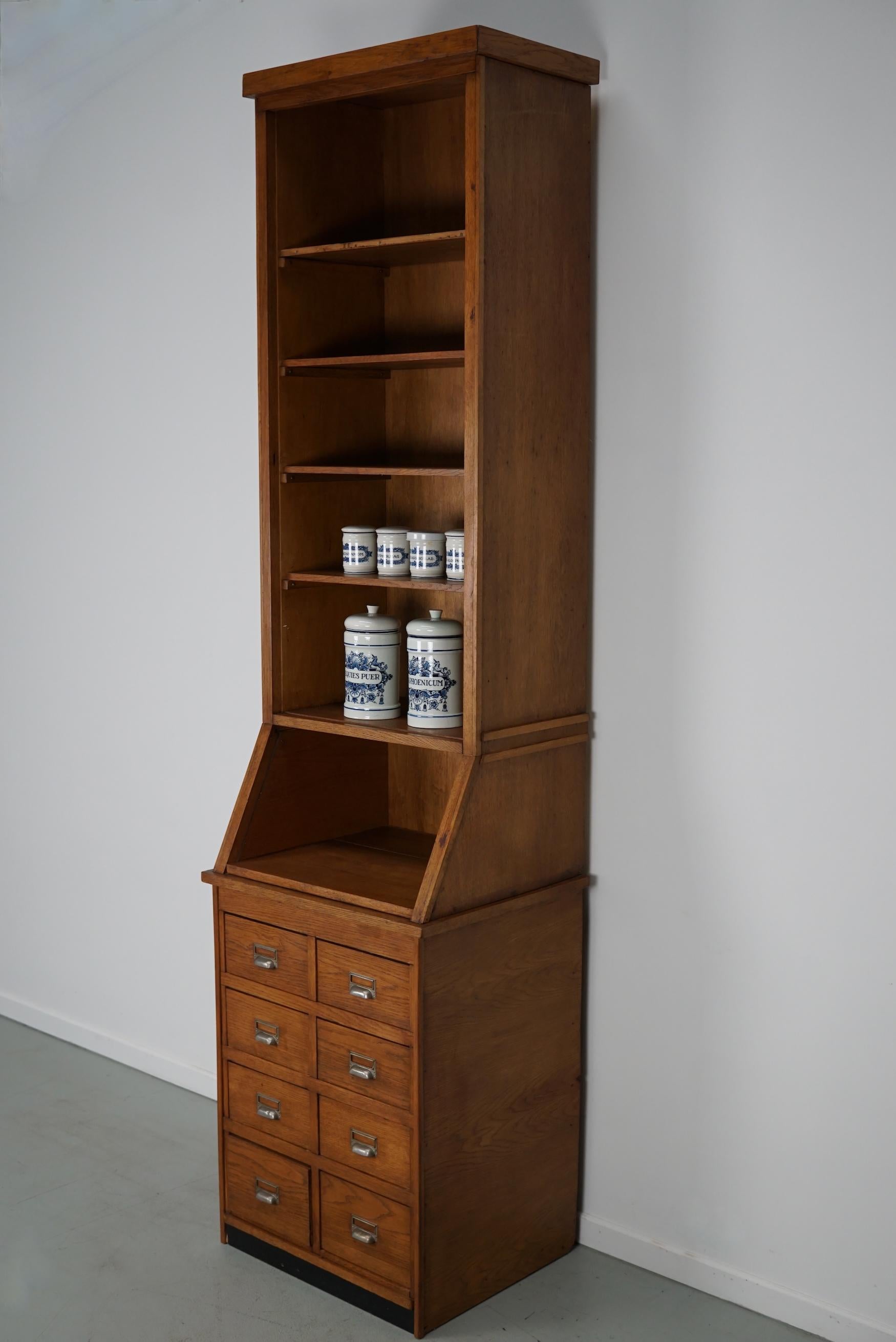 This shop cabinet was produced during the 1920/30s in the Netherlands. This piece features 8 drawers and 5 shelves and was made in two sections. It was originally used in a pharmacy in the early 20th century.