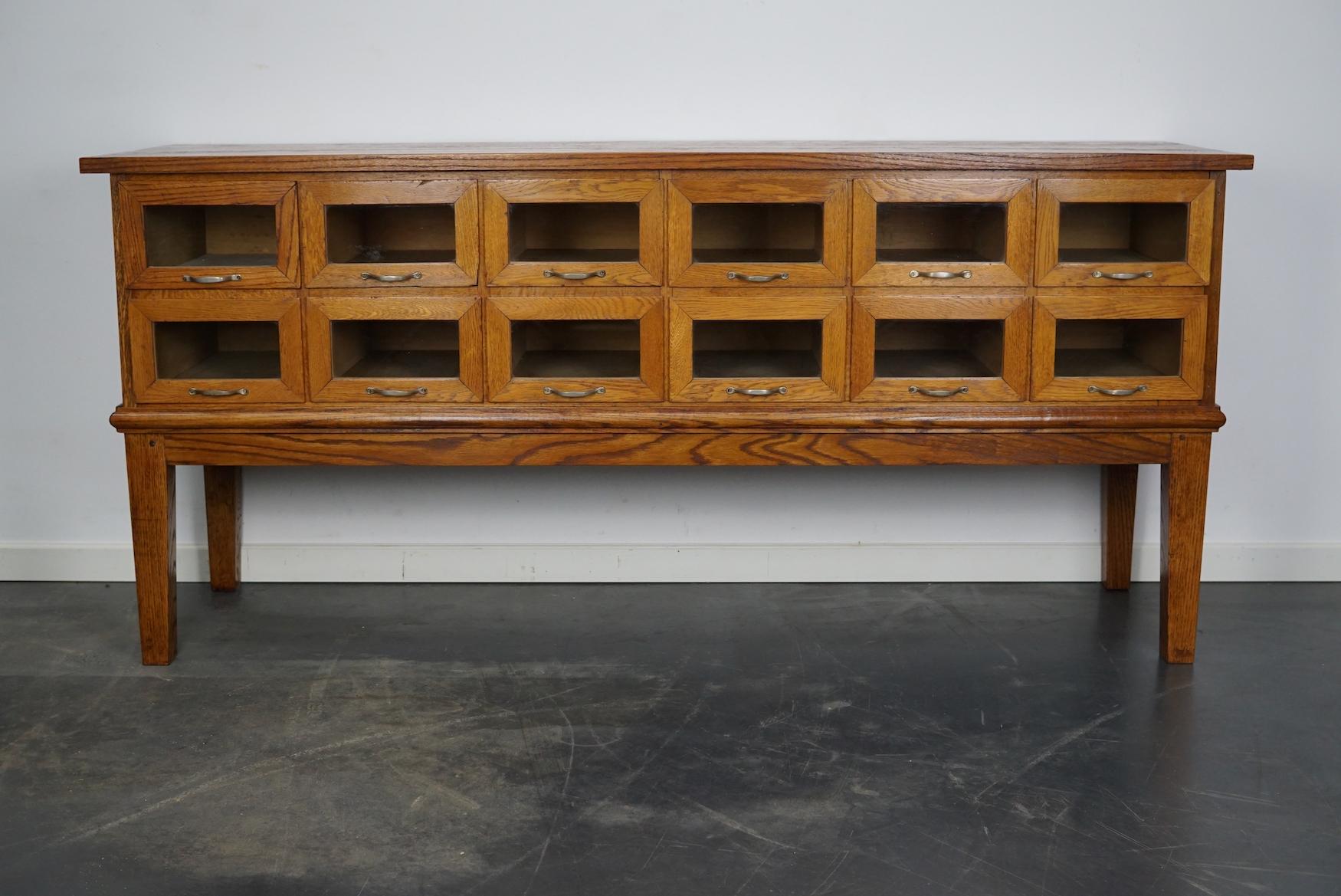 This haberdashery cabinet was produced during the 1950s in the Netherlands. This piece features 12 drawers in oak with glass fronts and metal handles. It was originally used in a luxury warehouse in the city of Maastricht. The interior dimensions of