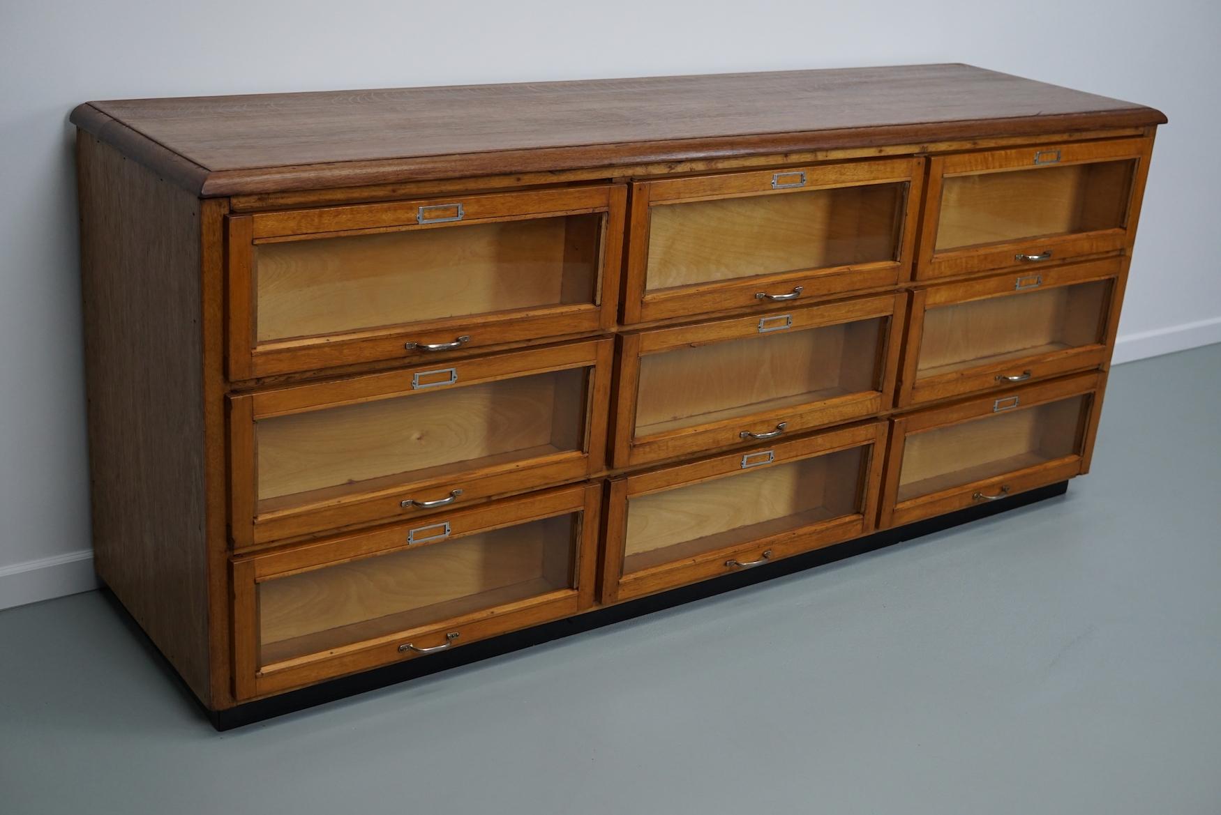This haberdashery cabinet was produced during the 1950s in the Netherlands. This piece features 9 large drawers in beech with glass fronts and metal handles. It was originally used in a luxury warehouse in the city of Maastricht. The interior