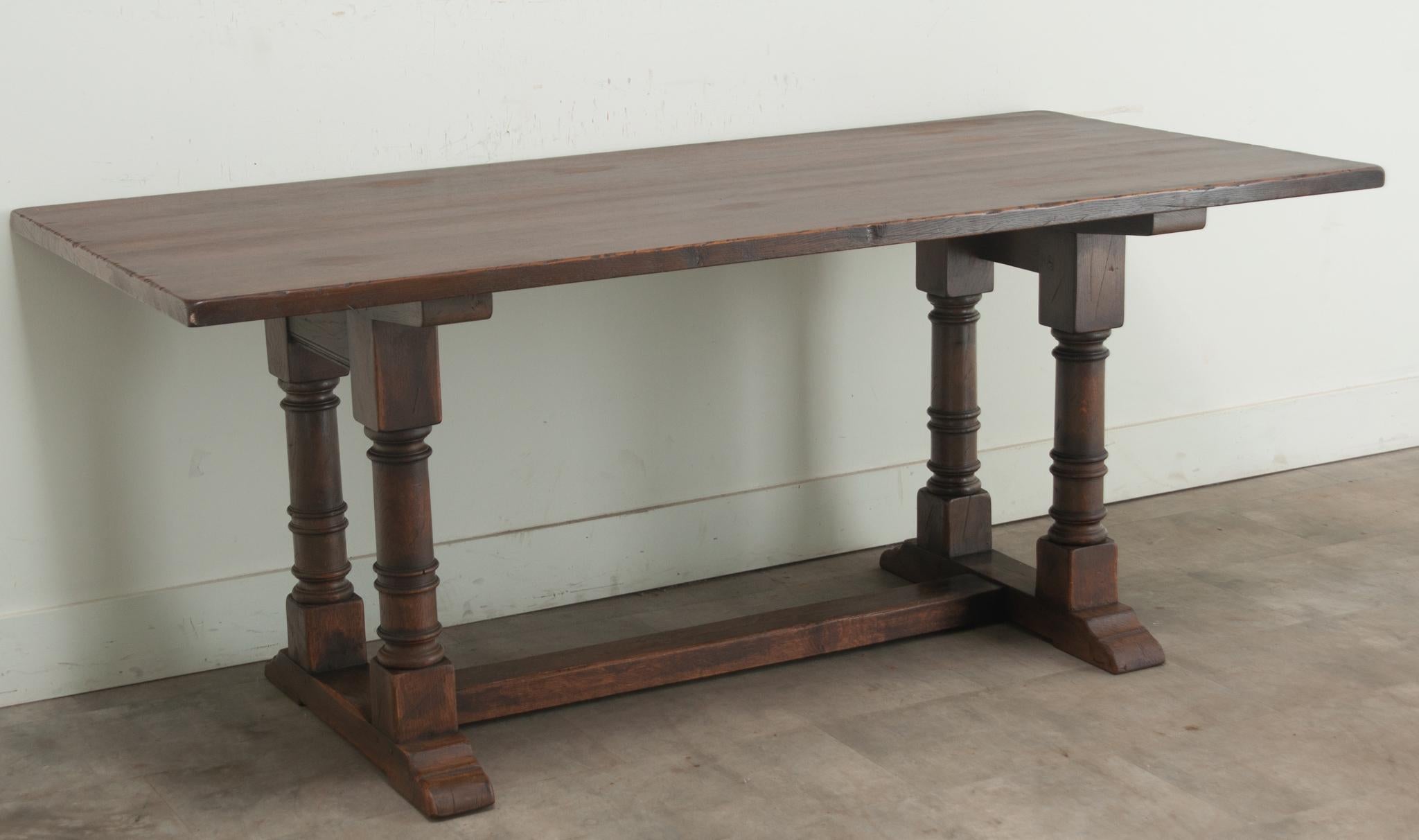 A vintage oak dining table from the Netherlands. This 1 ¼” thick single board table top rests over a trestle base composed of two turned baluster legs joined by a wide stretcher and base. This table has recently been cleaned and polished with a