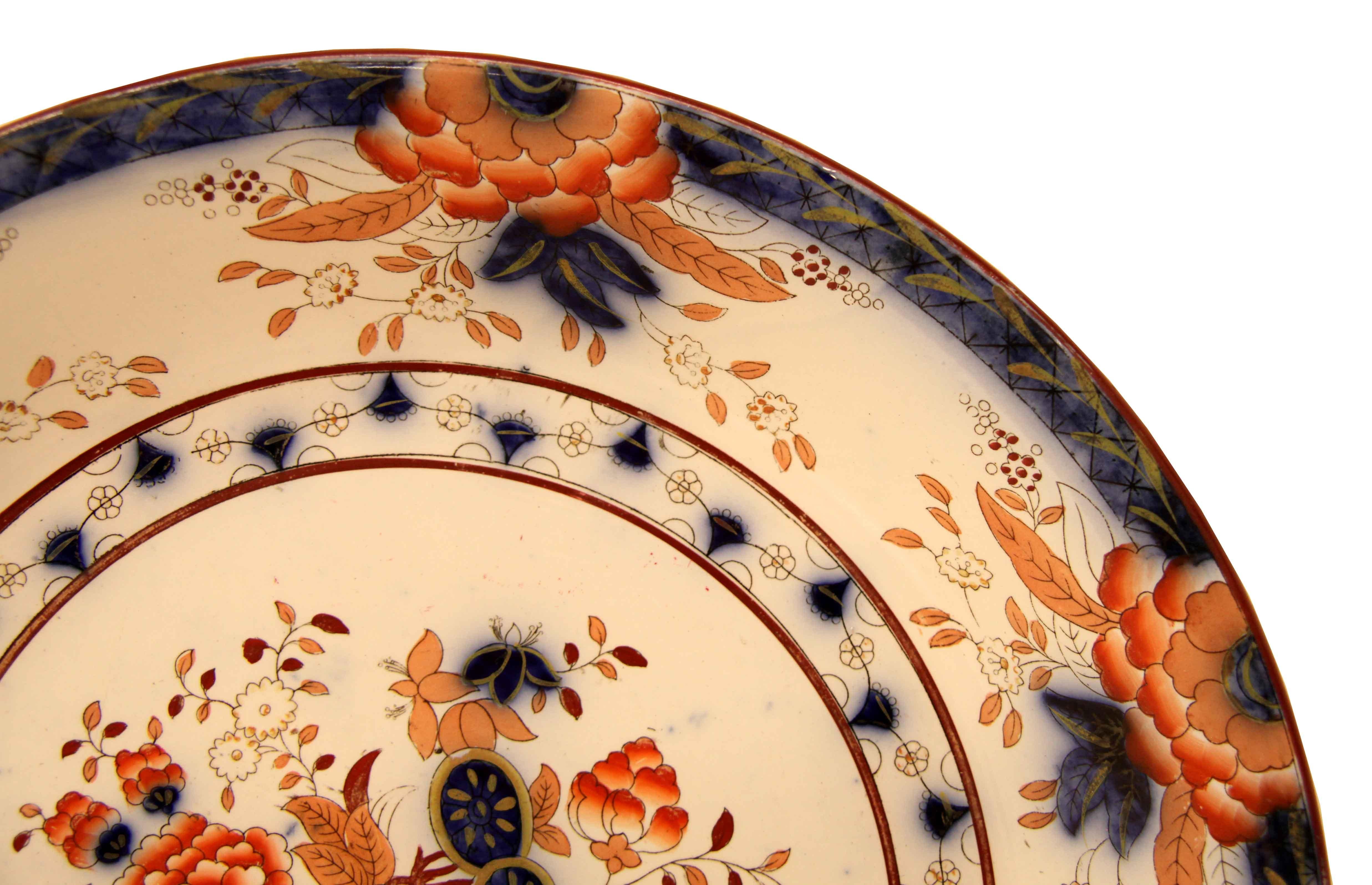 Dutch P. Regout charger,, the outer edge has a flow blue background with foliate , this is separated a repeated design of various stylized flowers and foliate in shades of orange, coral, tan, and flow blue.  The center features a flow blue urn with