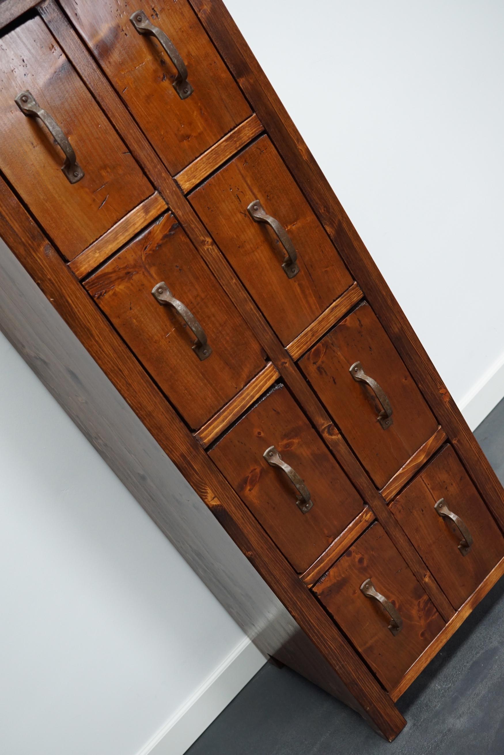 This cabinet was produced during the 1930s in the Netherlands. It was used in a factory for yeast and spirits which is also visible on the inside of the drawers as the back of the drawers were made from old factory crates. This piece features 8 pine