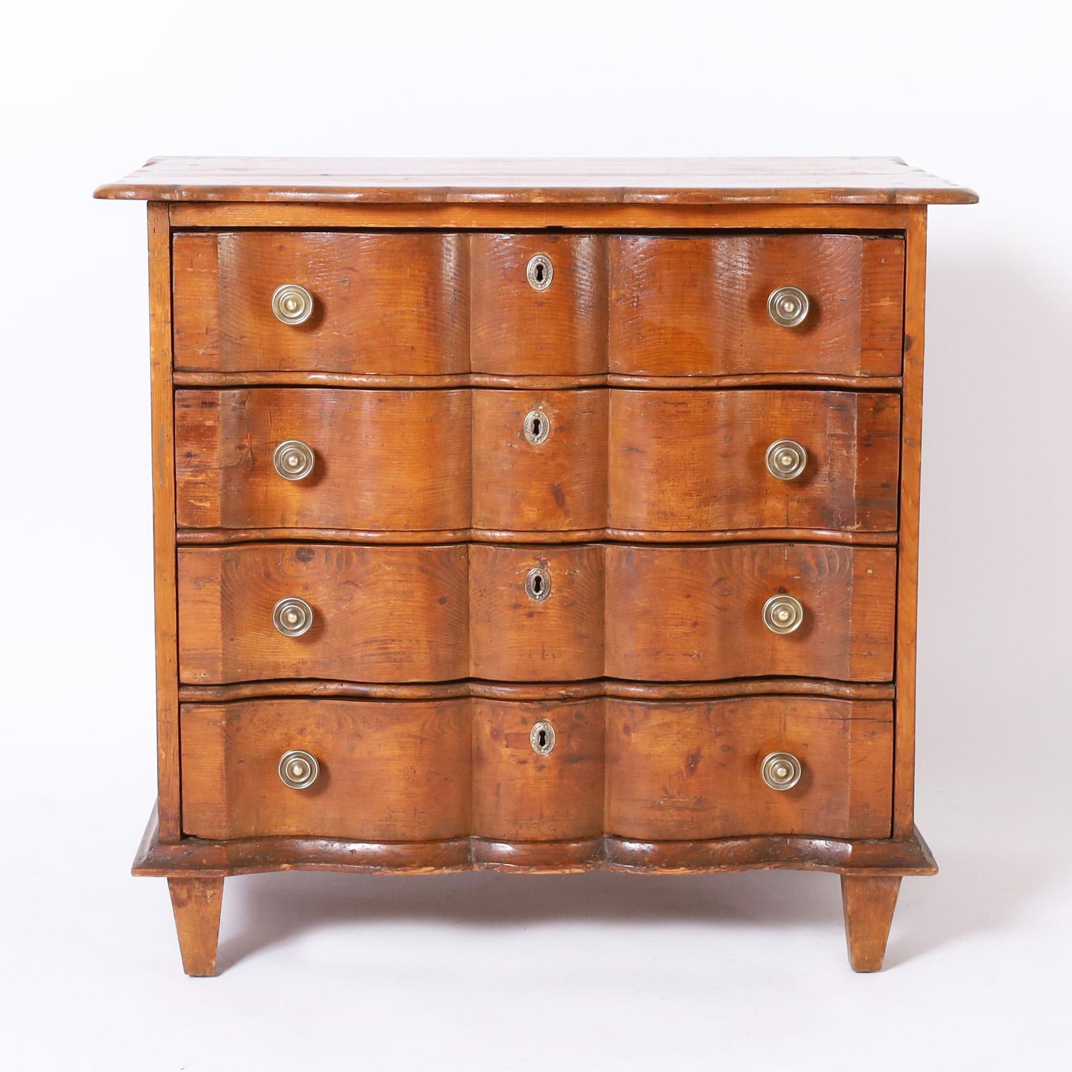 Rare and remarkable 18th century Dutch cottage commode handcrafted in pine with four drawers having a scalloped top over a dramatic serpentine form case with a centuries old patina, brass hardware, and front tapered legs.