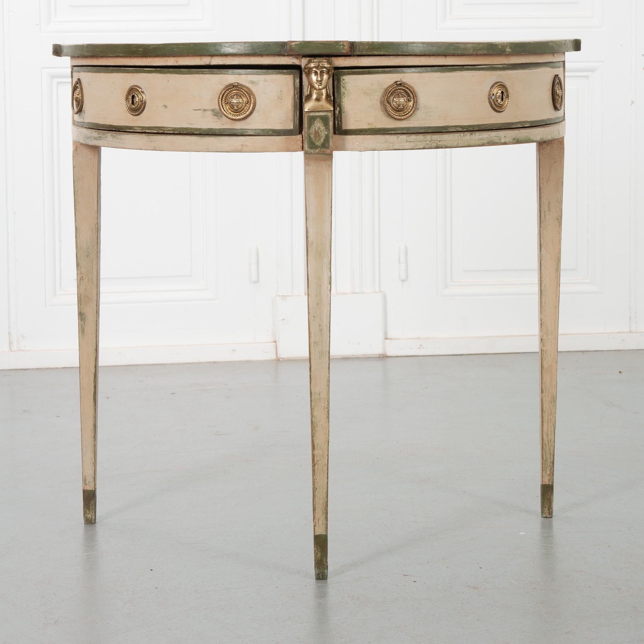 This Dutch Regency 19th century console is just as much of a work of art as it is a working table. Painted mostly cream with accents of earthy green, this is a perfect conversation piece for a small space. The shaped top is fixed to a two drawered