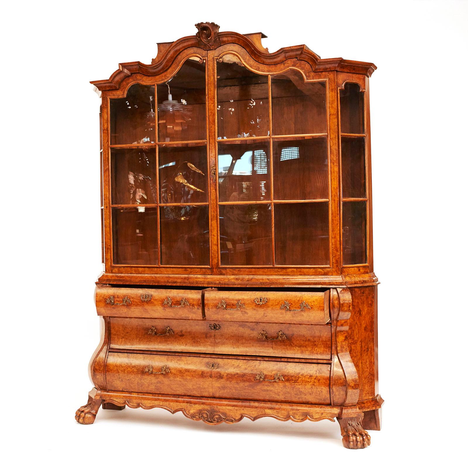 A Dutch Rococo bookcase burl walnut cabinet, circa 1770s, in two parts.

The arched and curved cornice molding above two glazed doors, the lower section with two short drawers above two long drawers of bombé form.
The sides with extended scrolls and