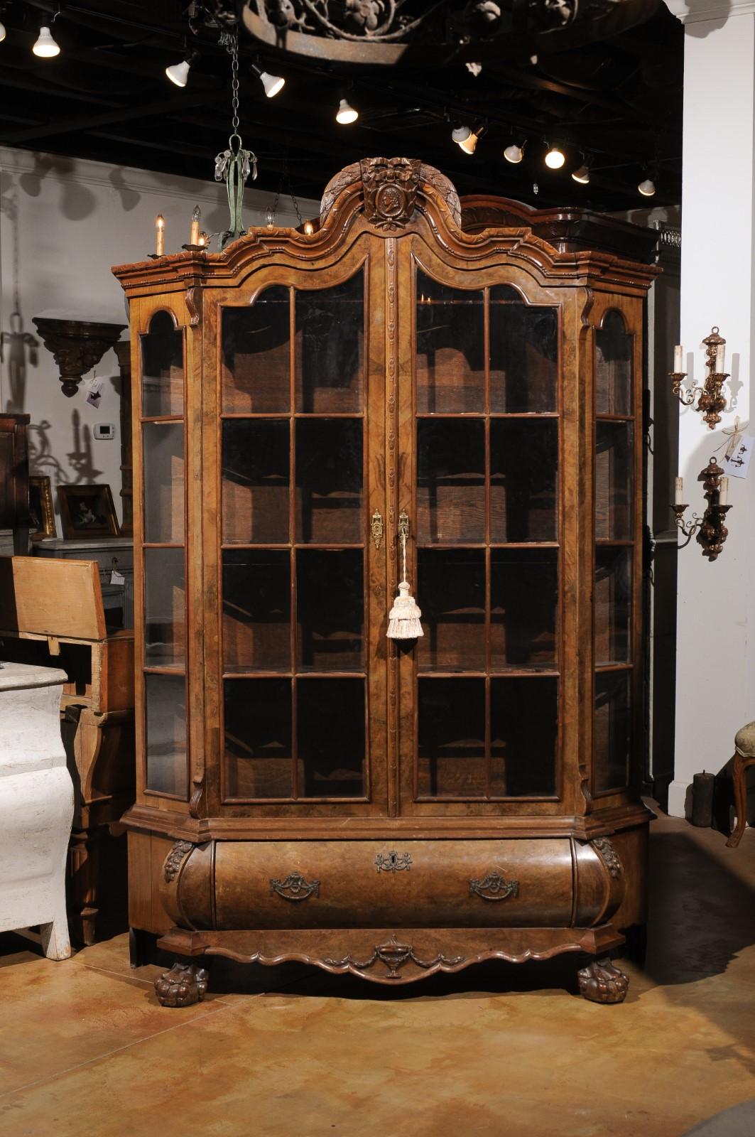 A Dutch walnut Rococo Revival bombé vitrine from the late 19th century, with glass doors and single drawer. Created in the Netherlands during the last decade of the 19th century, this wooden vitrine, adorned with a bonnet type pediment, features