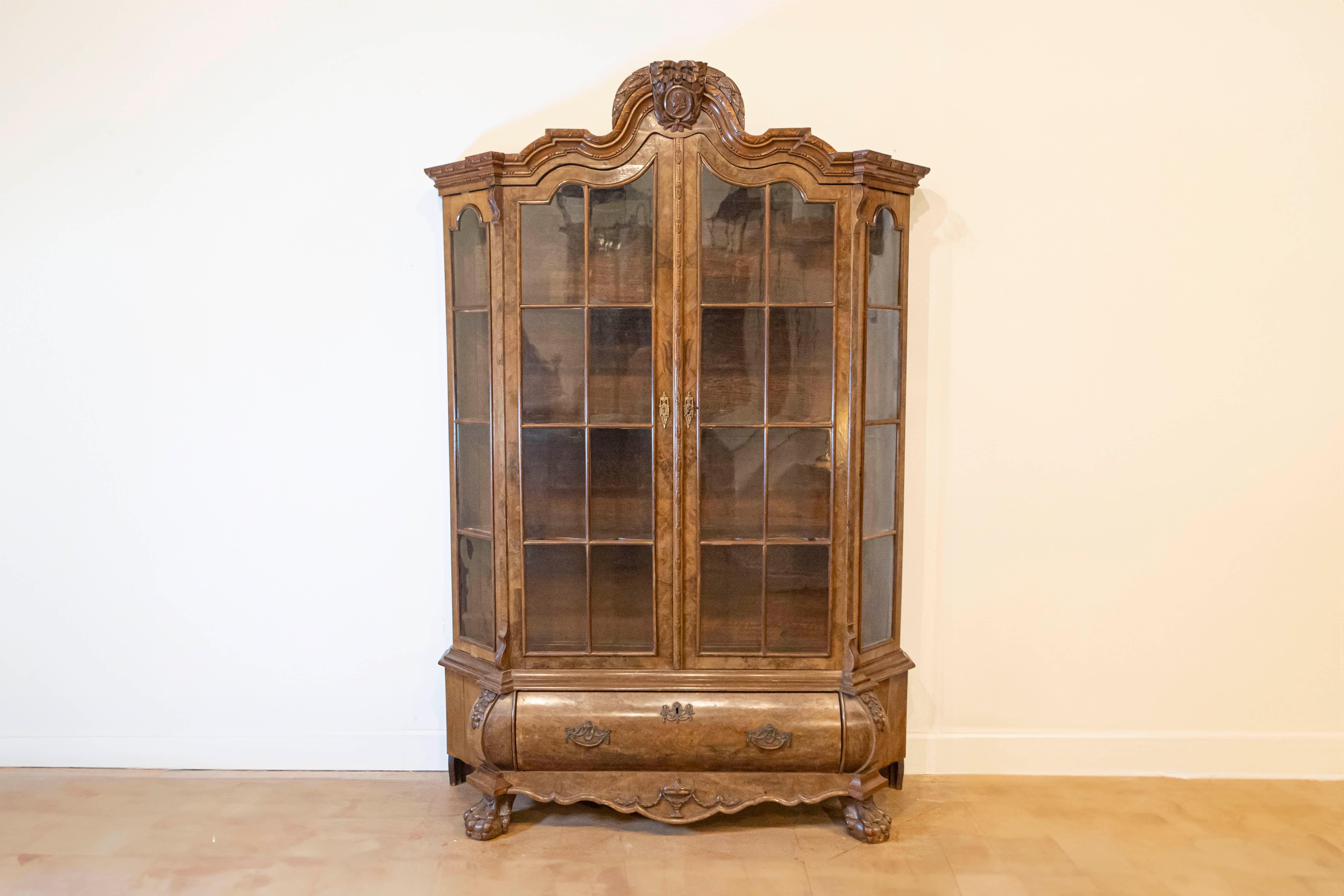 A Dutch walnut Rococo Revival bombé vitrine from the late 19th century, with glass doors and single drawer. Created in the Netherlands during the last decade of the 19th century, this wooden vitrine, adorned with a bonnet type pediment, features
