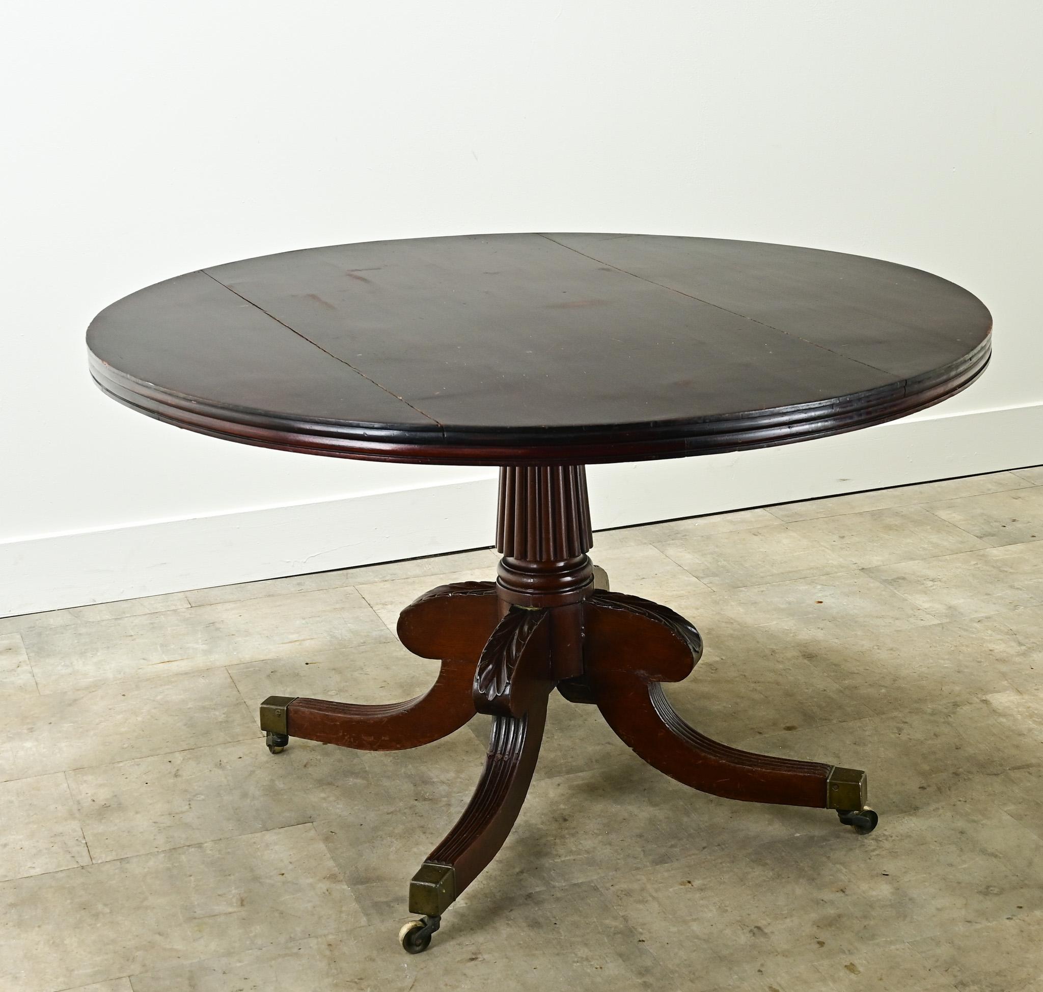 The perfect round dining table to comfortably seat four people. This dutch tilt top table is made of mahogany and has the ability to tilt upright. The pedestal base has a reeded center style with four shaped and carved splayed legs ending on brass