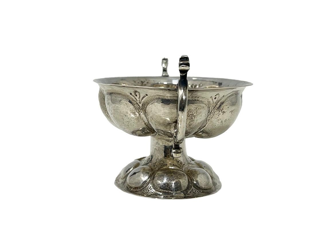 Cuenco pequeño de plata holandesa de Heerens, Schoonoven, 1956

Pequeño cuenco holandés de plata, de forma ovalada martillada y lobulada, elevado sobre un pie lobulado ovalado con dos orejas con volutas y una cabeza de cisne a cada lado y varios