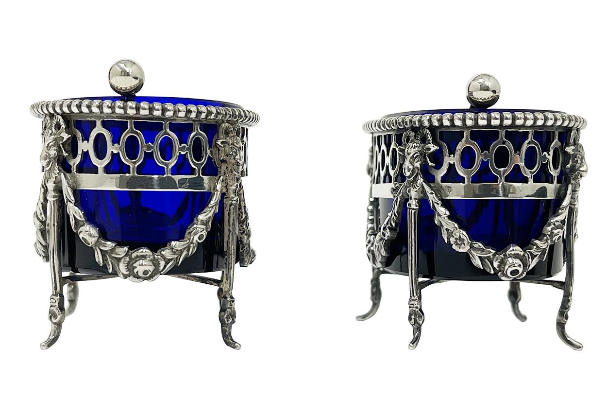 Dutch Silver with blue crystal glass salt cellars by P. Heerens, 1902-1905

Two salt cellars raised on 4 small fluted Empire style legs with above a rams head between floral guirlandes.  The two salt cellars, made of Dutch silver and inside blue
