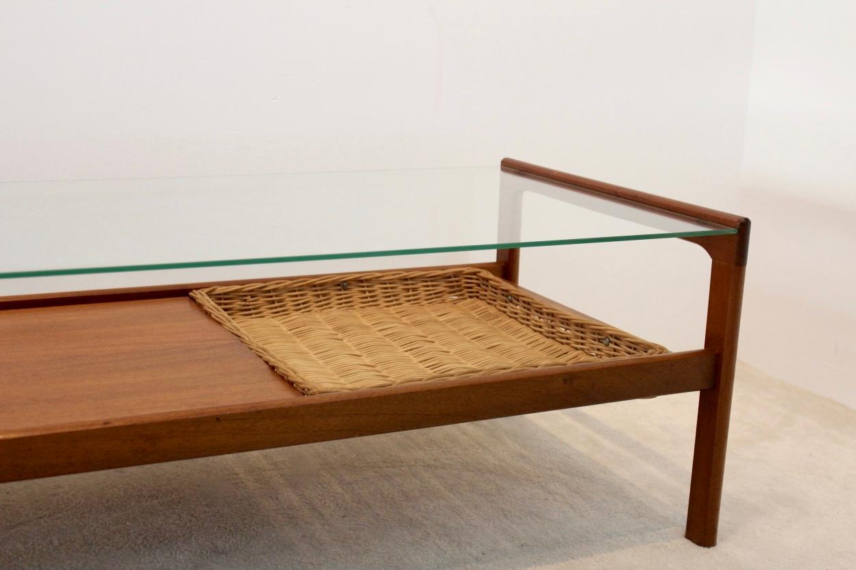 This beautiful teak midcentury coffee table features two tiers: one glass top and one teak shelf with a sophisticated Wicker inlay. This piece makes a great addition to home or business. Made of teak and in very good condition.
