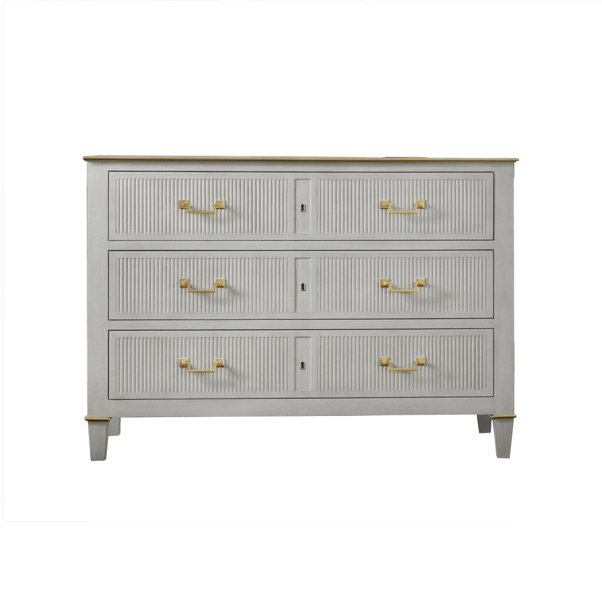 The Transitional Painted Commode is fitted with three long drawers and has an antiqued painted finish. With brass molded trim, the design features fluted drawer fronts and side panels, with solid brass Neo Classic drawer pulls and raised on short