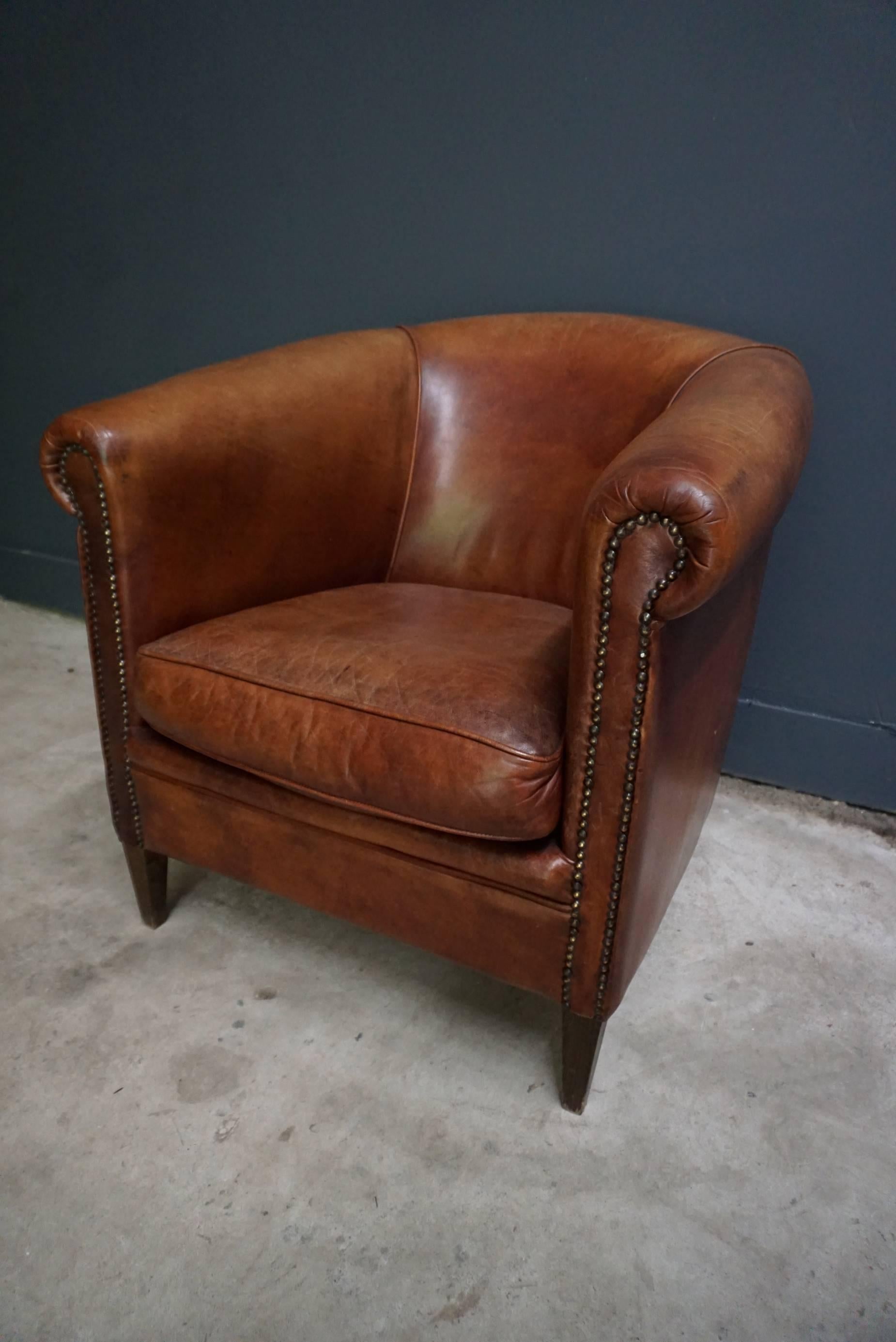 This vintage club chair is upholstered with cognac-colored leather and features metal pins and wooden legs.