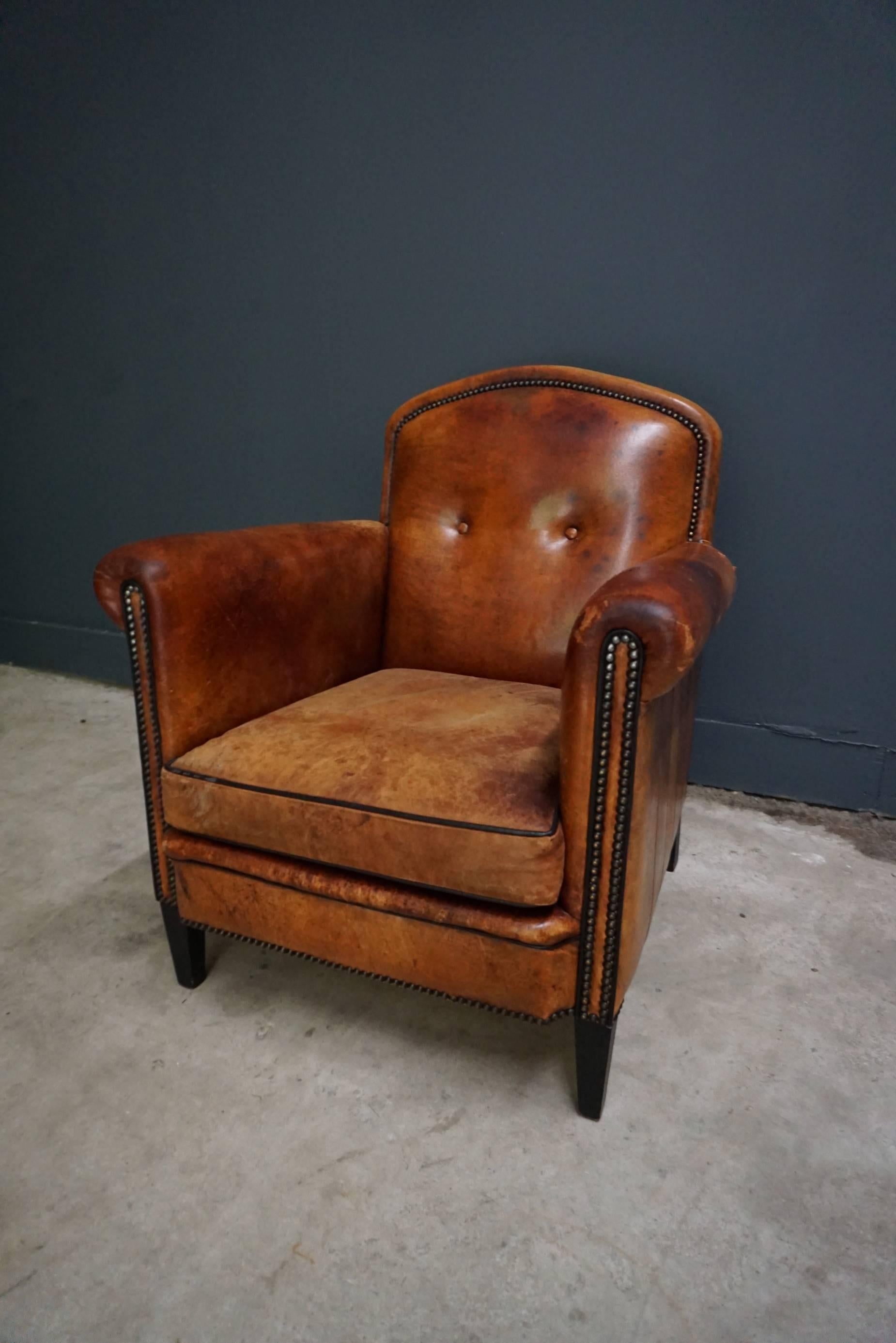 This vintage club chair is upholstered with cognac-colored leather and features metal pins and wooden legs.