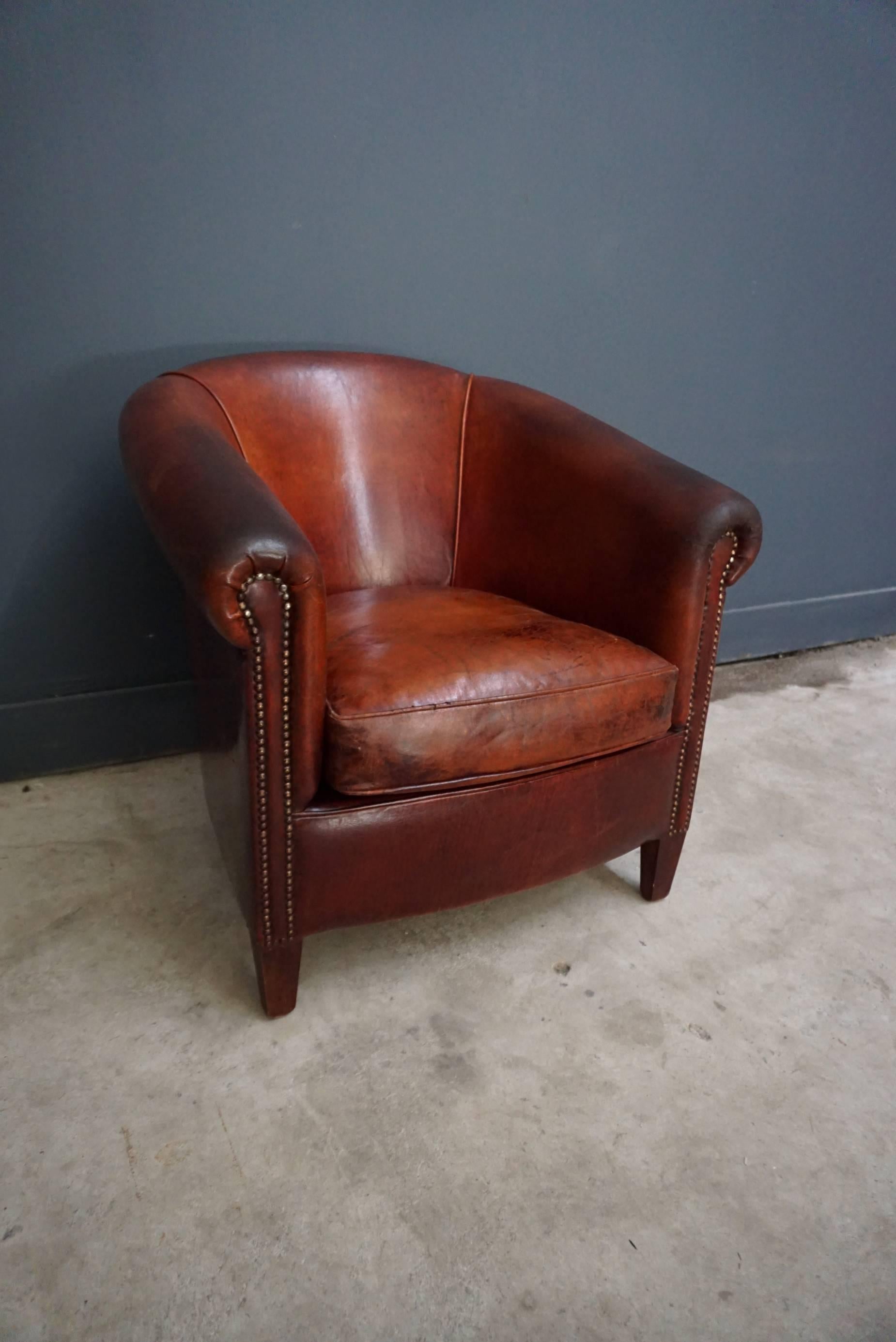 This vintage club chair is upholstered with cognac-colored leather and features metal rivets and wooden legs.