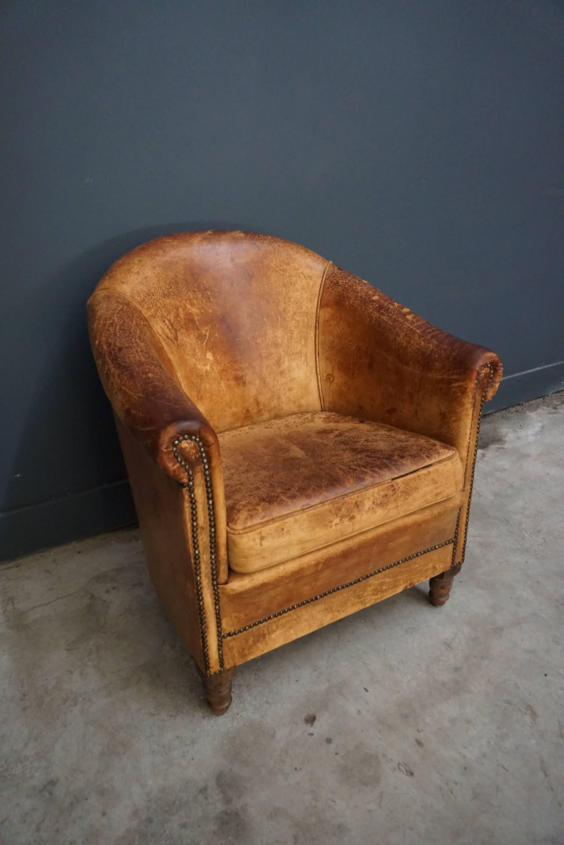 Dieser Vintage-Clubsessel ist mit cognacfarbenem Leder gepolstert und verfügt über Metallnieten und Holzbeine.