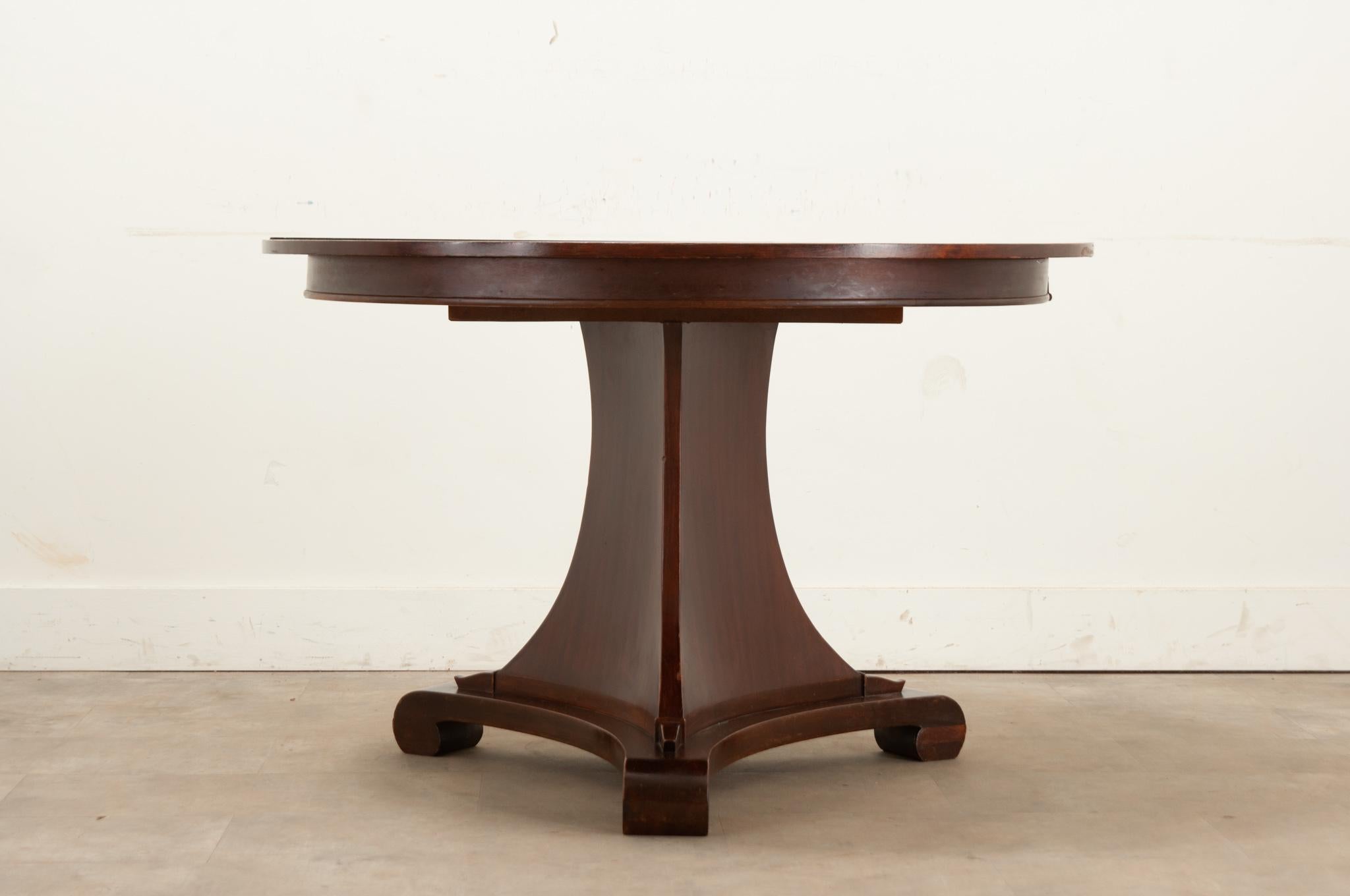 A vintage extending table made from mahogany made in France. This table has a simple top that rests above a pedestal base on scroll feet. The tabletop opens to accommodate one leaf in the middle, adding 15 ¾”W. Cleaned and polished with a French