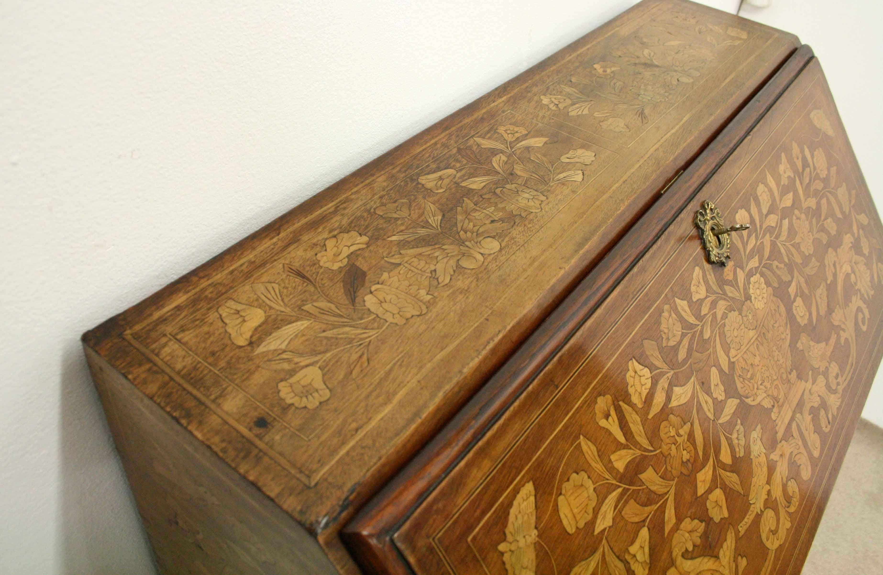 Dutch walnut marquetry inlaid bureau, circa 1860. The flap has a large marquetry urn with flowers spilling out of it at both sides, butterflies and birds. There is a very stylish cast brass gilded escutcheon with the aperture for the key and swags
