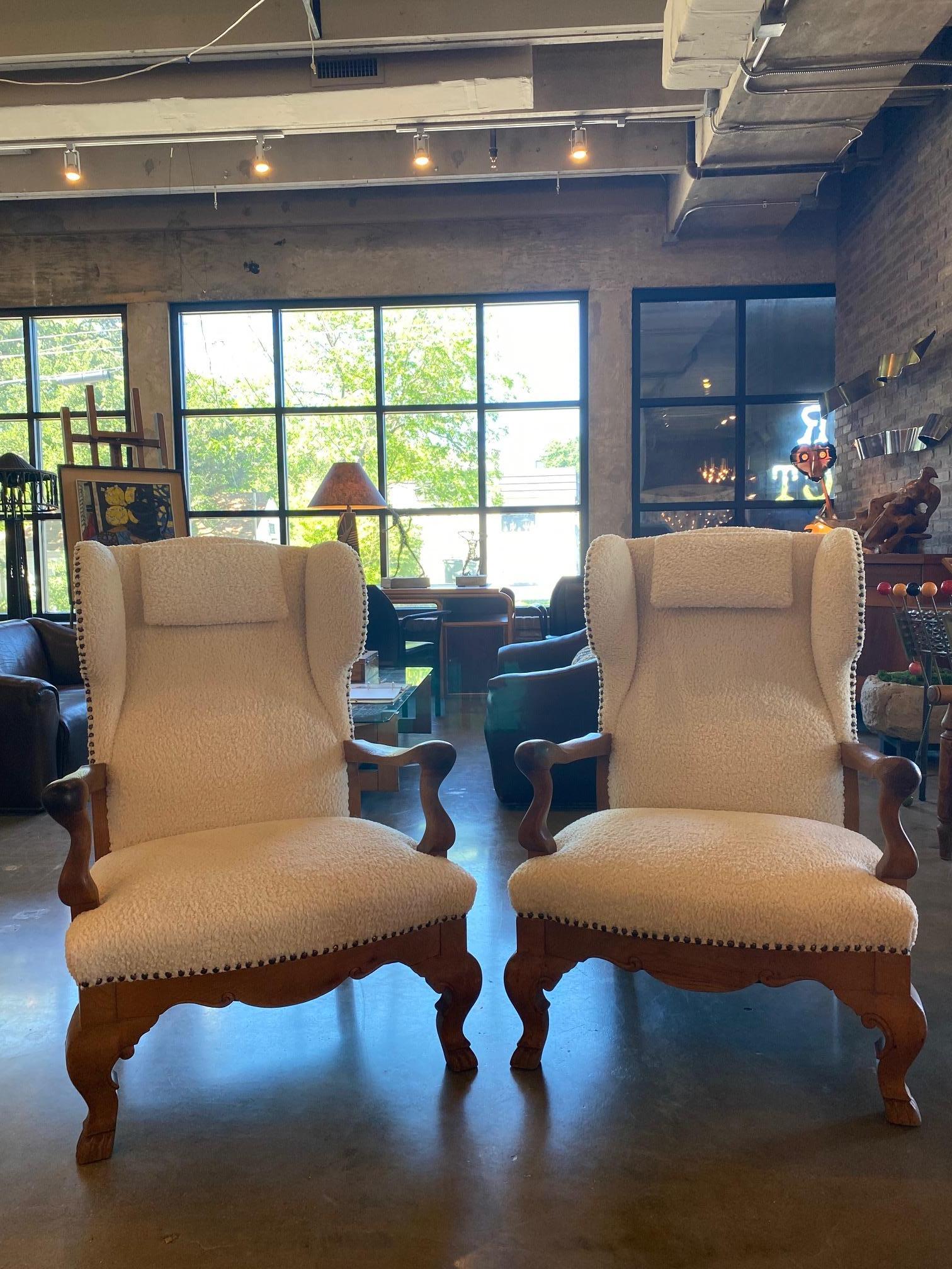 Pair of early-mid 20th century Dutch wingback chairs in solid oak with sculptural details reminiscent of French designers Guillerme et Chambron. New custom off-white boucle upholstery and bronze nail heads allow the chairs to present in almost