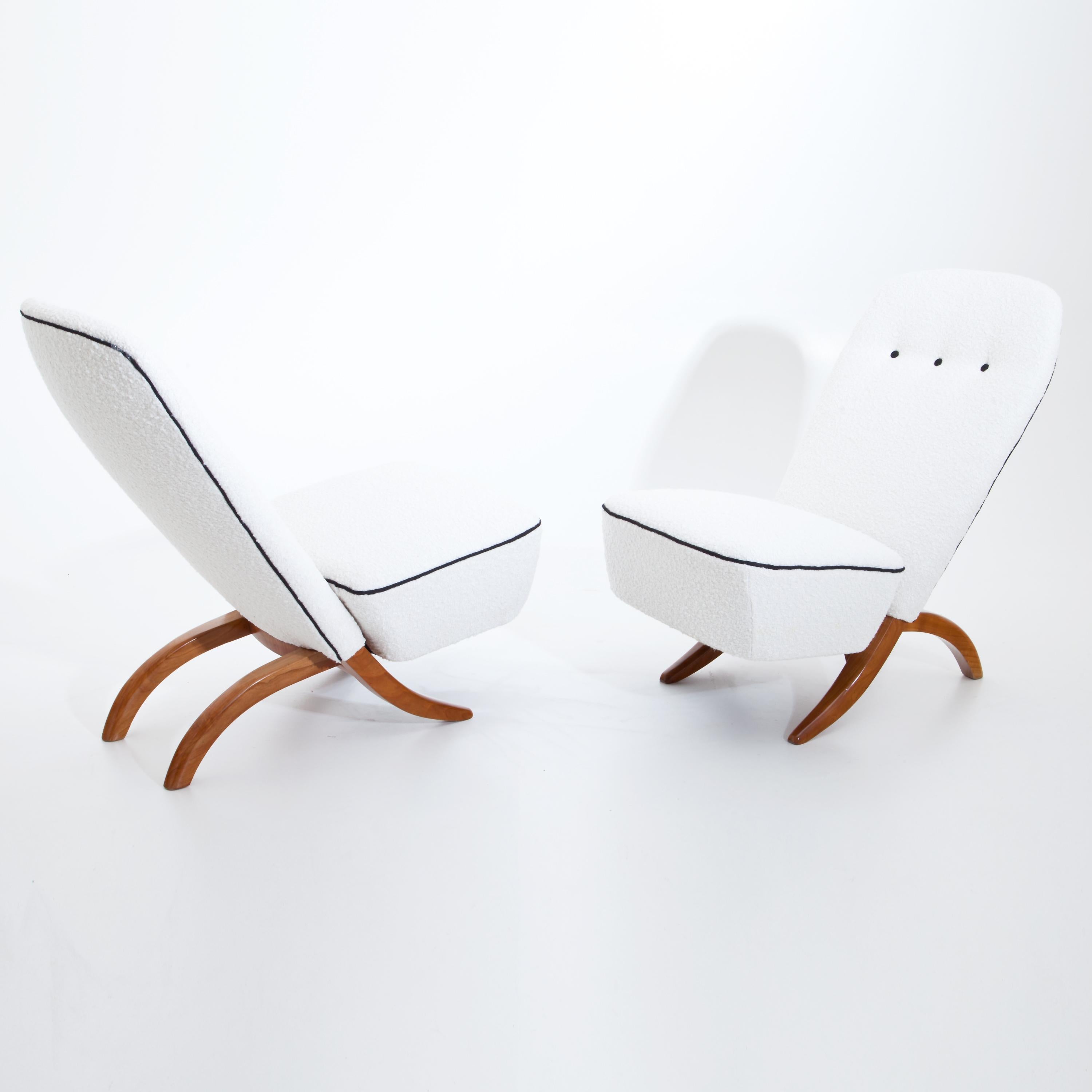 Pair of lounge chairs on curved feet out of cherry wood. The strongly inclined, rounded backrest and seat are newly covered with a white bouclé fabric with black piping and buttons.