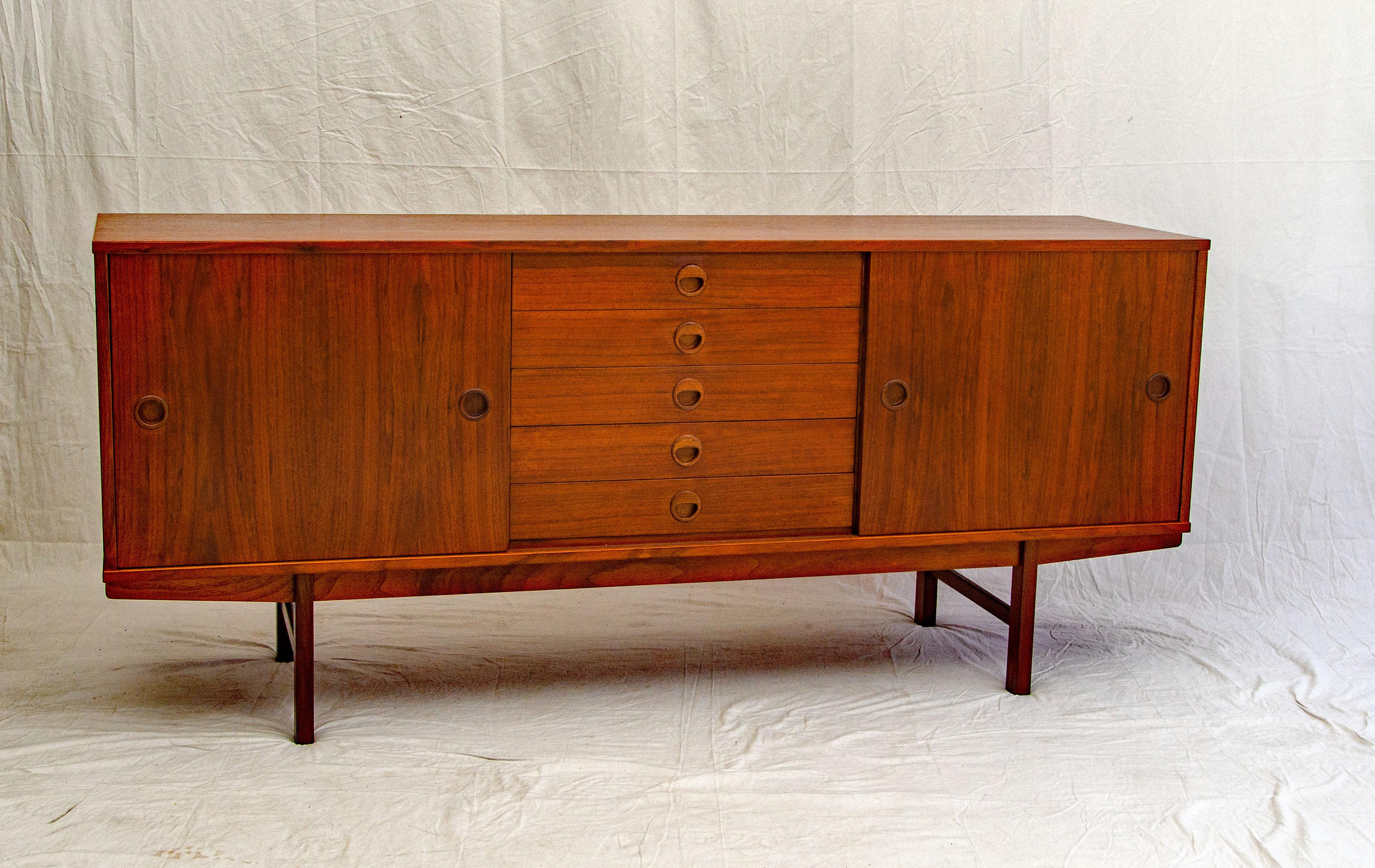 This walnut credenza by DUX of Sweden has five drawers, two sliding doors, and a sled base. There are two adjustable shelves that slide in and out on wire supports. DUX signature on the base.