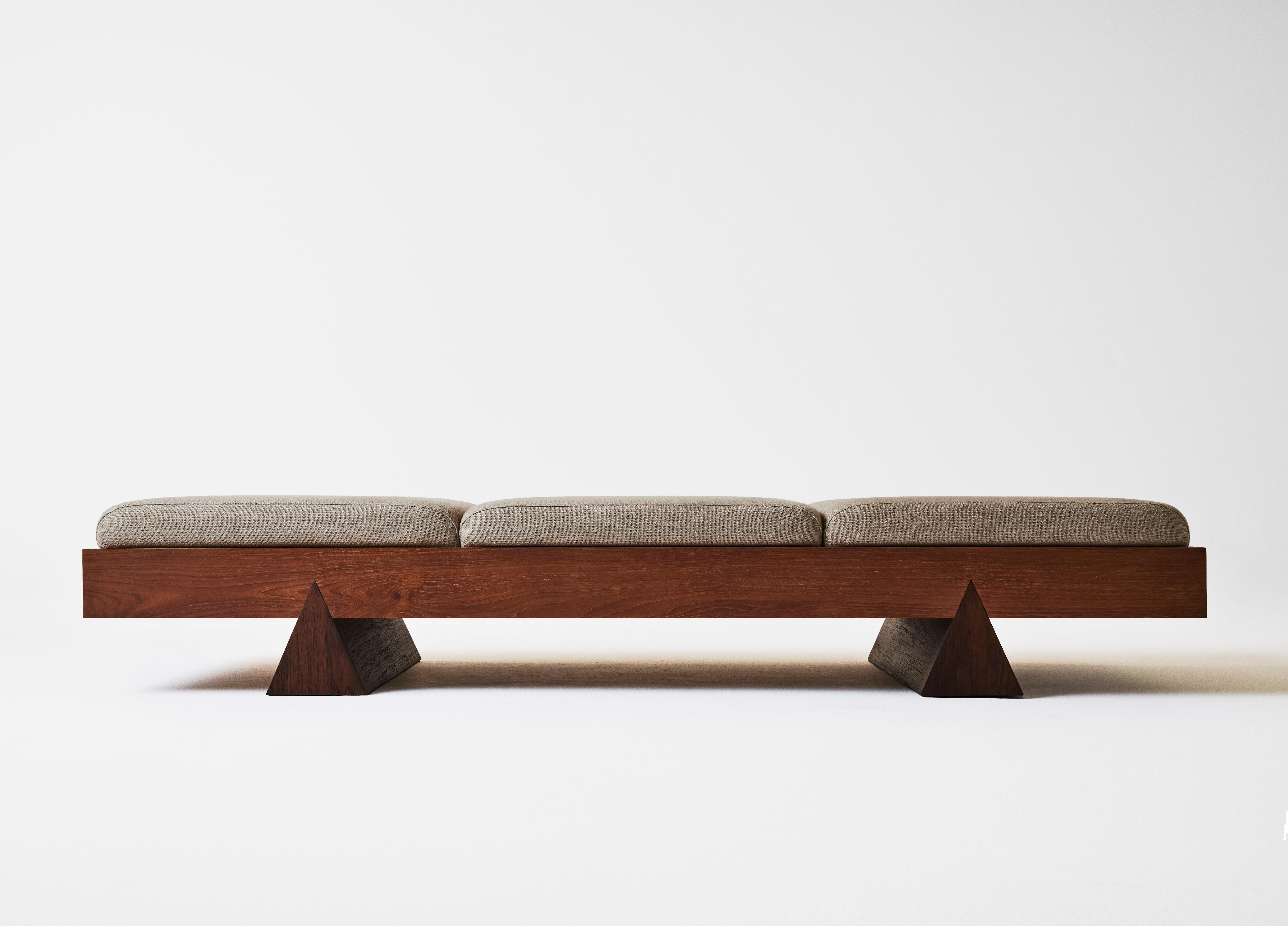 The Dvaya Bench embodies duality through its thoughtful design where contrast and equilibrium coalesce. This piece exhibits an intriguing play on scale, where a substantial wooden frame is gracefully supported by triadic legs. The generous seating