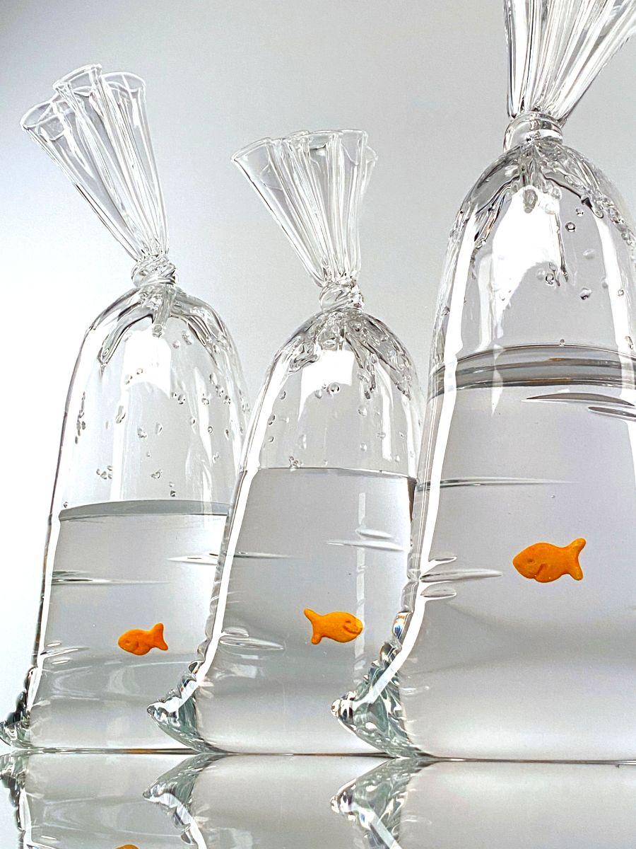 Die limitierte Auflage dieser hyperrealen Goldfisch-Cracker-Wassertüten aus Glas ist eine verspielte Anspielung auf die Karnevals-Goldfische in Plastiktüten. 

Jedes Stück, das mit geschmolzenem Glas bei über 2000° F hergestellt wird, ist