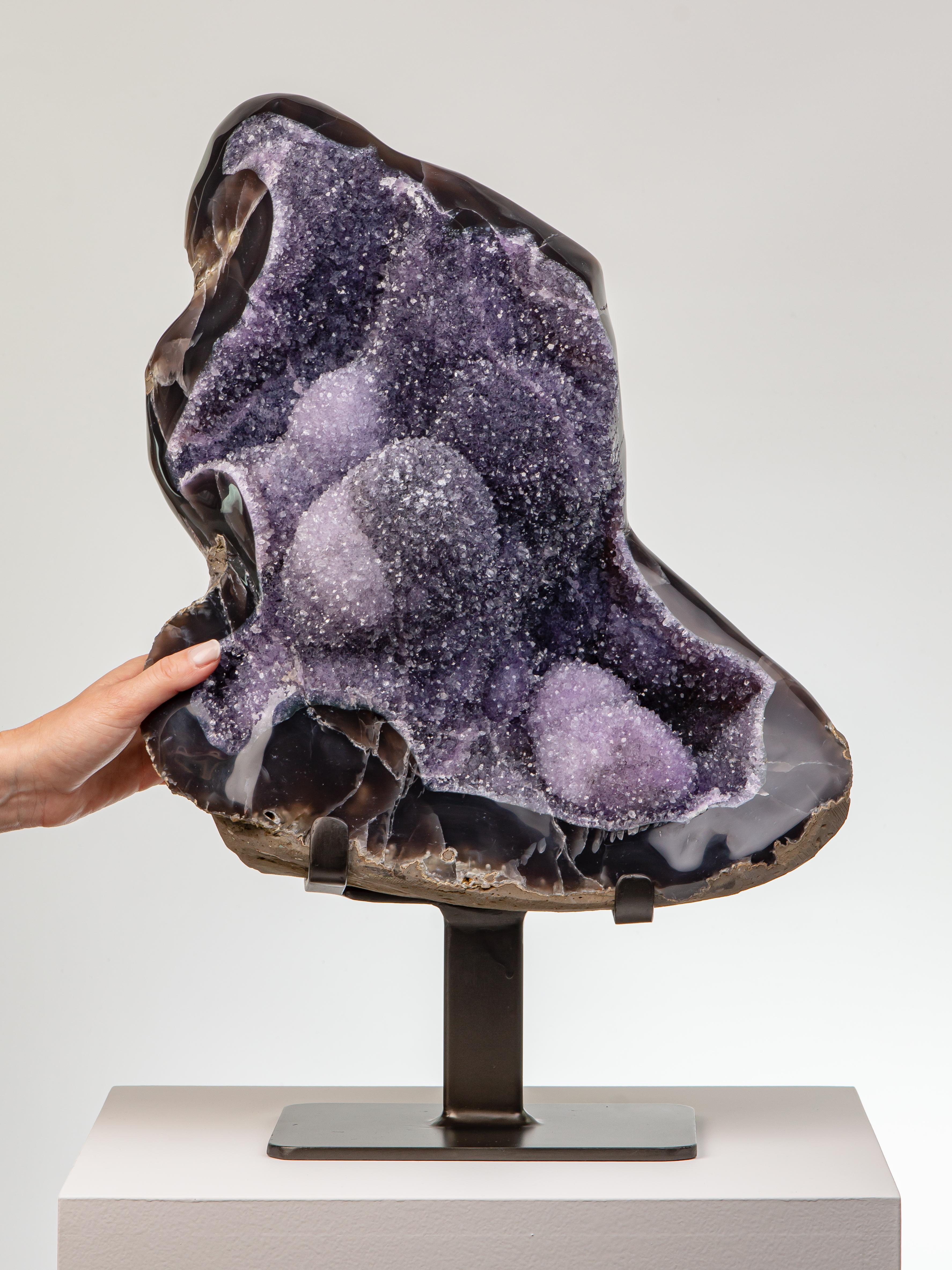 A dynamic formation with a thick blue-brown agatised border. The crystal
lined interior equally dynamic with shocks of electric amethyst contrasting
with darker colours on a bed of large stalactites.

This piece was legally and ethically sourced
