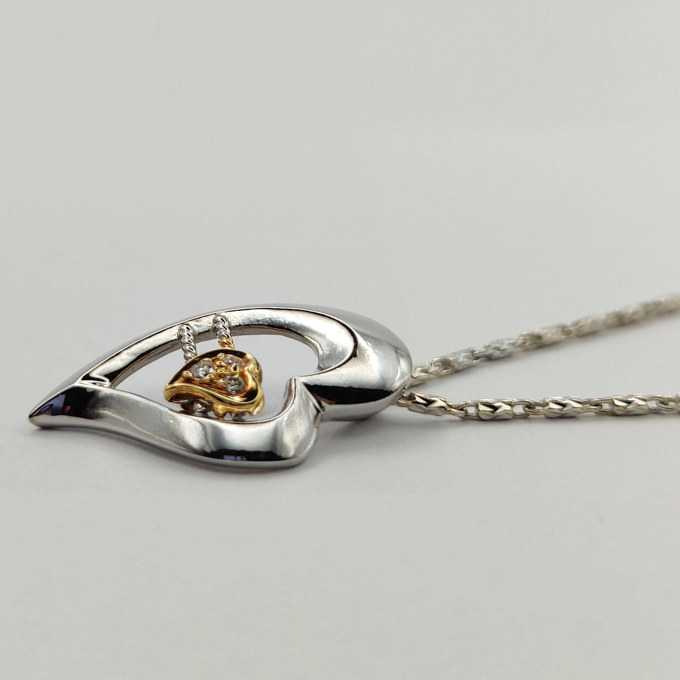 The Dynamic Heart Diamond Pendant is a stunning and unique piece that is sure to catch the eye. The pendant features a large white gold heart with a smaller yellow gold heart nestled inside. The smaller heart is encrusted with 3 sparkling diamonds,