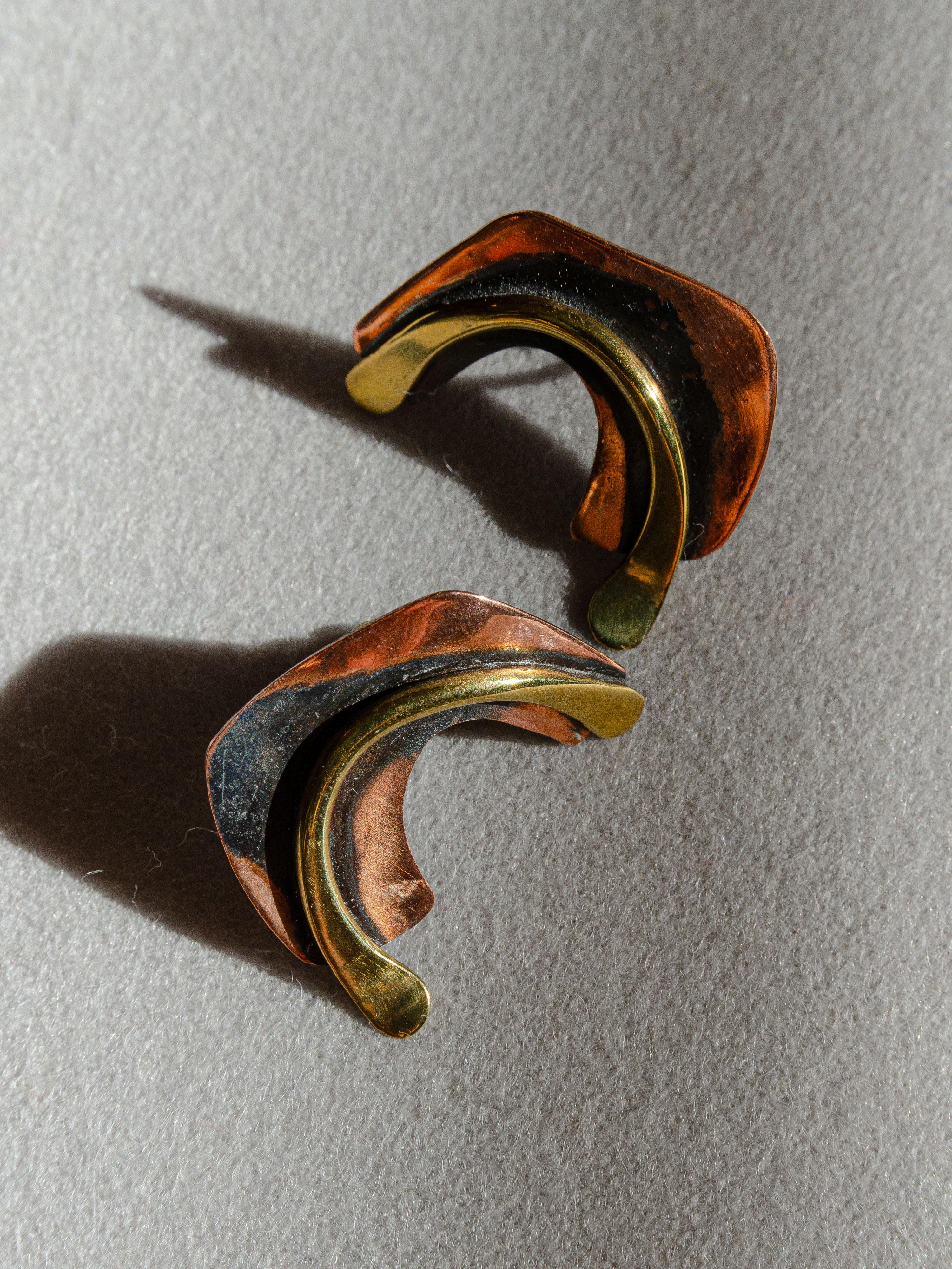 A graceful pair of copper and brass biomorphic earrings designed by Greenwich Village modernist jeweler Art Smith in the 1950's. Smith is considered a master jewelers during the modernist movement of the mid-twentieth century.   

Fusing eclectic
