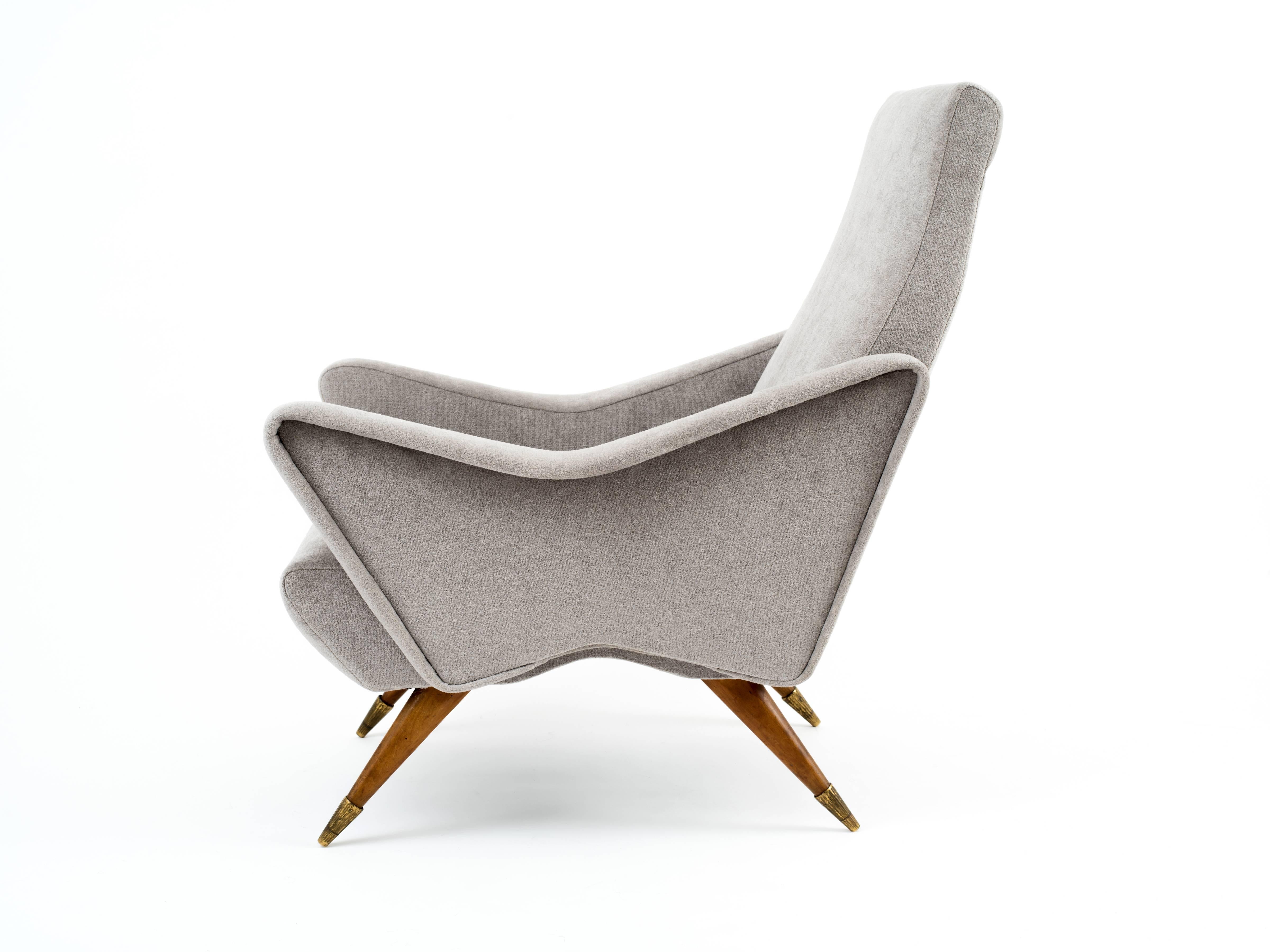 A pair of Italian mid century lounge chairs with dynamic-yet-elegant profiles. Fruitwood legs and fluted, solid brass sabots with rich patina add an organic flare and contrast beautifully against the cloud-gray, textured cotton upholstery. A rare