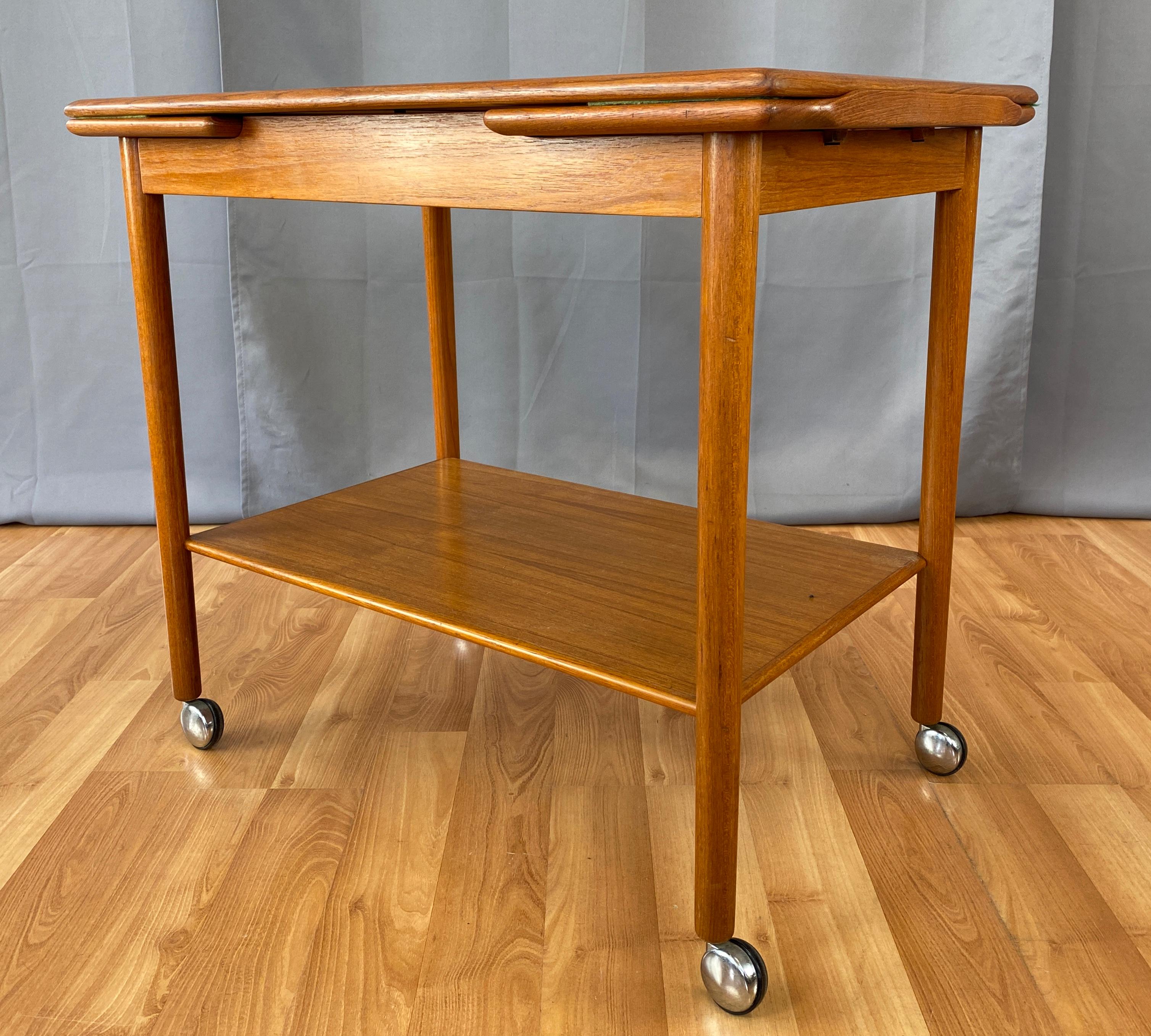 Offered here is a circa 1960s Teak bar and/or tea cart, by Dyrlund Denmark.
Four chrome casters, a large Teak bottom shelf, over this is the Teak top shelf which has two pull outs under it.
The pullouts, one side is Teak with the other has a black