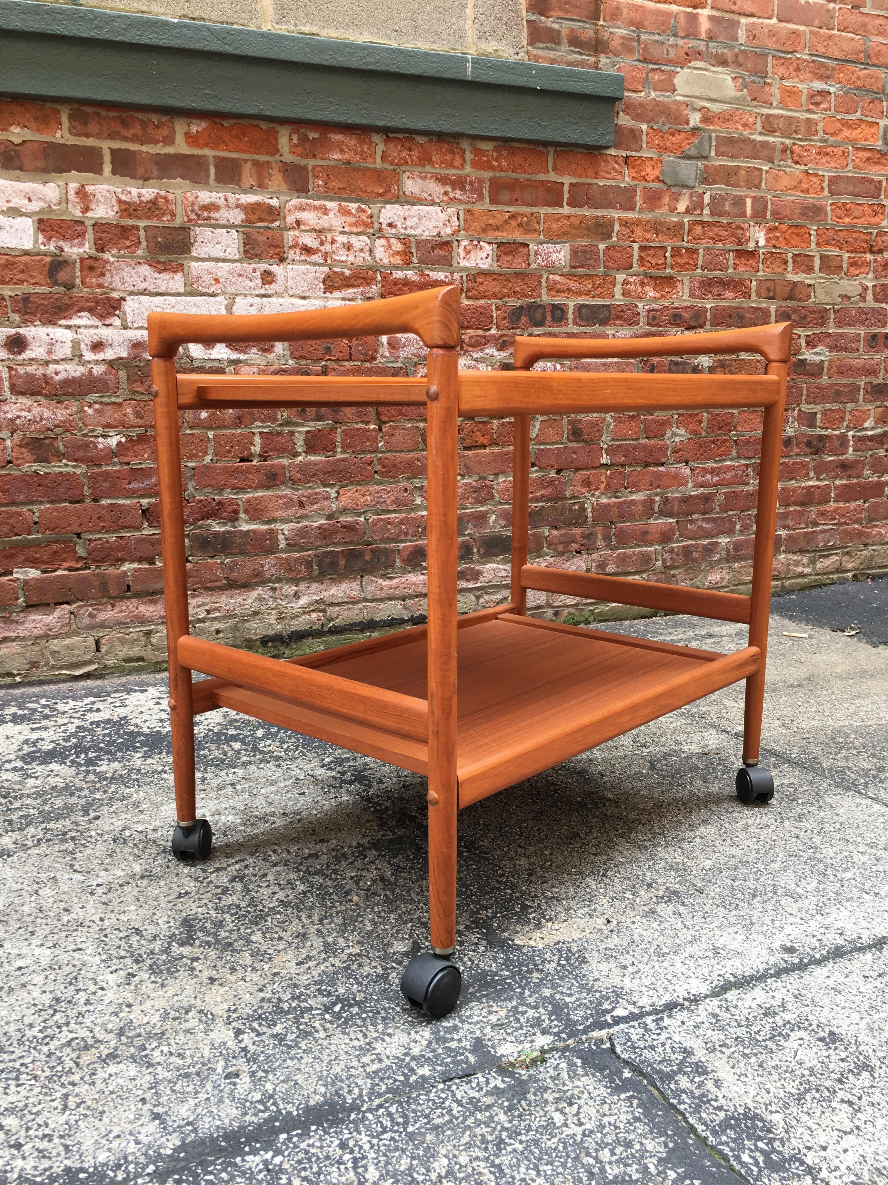 Dyrlund Danish teak rolling serving/media cart. The perfect Danish modern cart for a small flat screen TV, bric brac or rolling bar cart, circa 1970-1980. Black plastic casters. Very clean original condition. Signed on bottom.