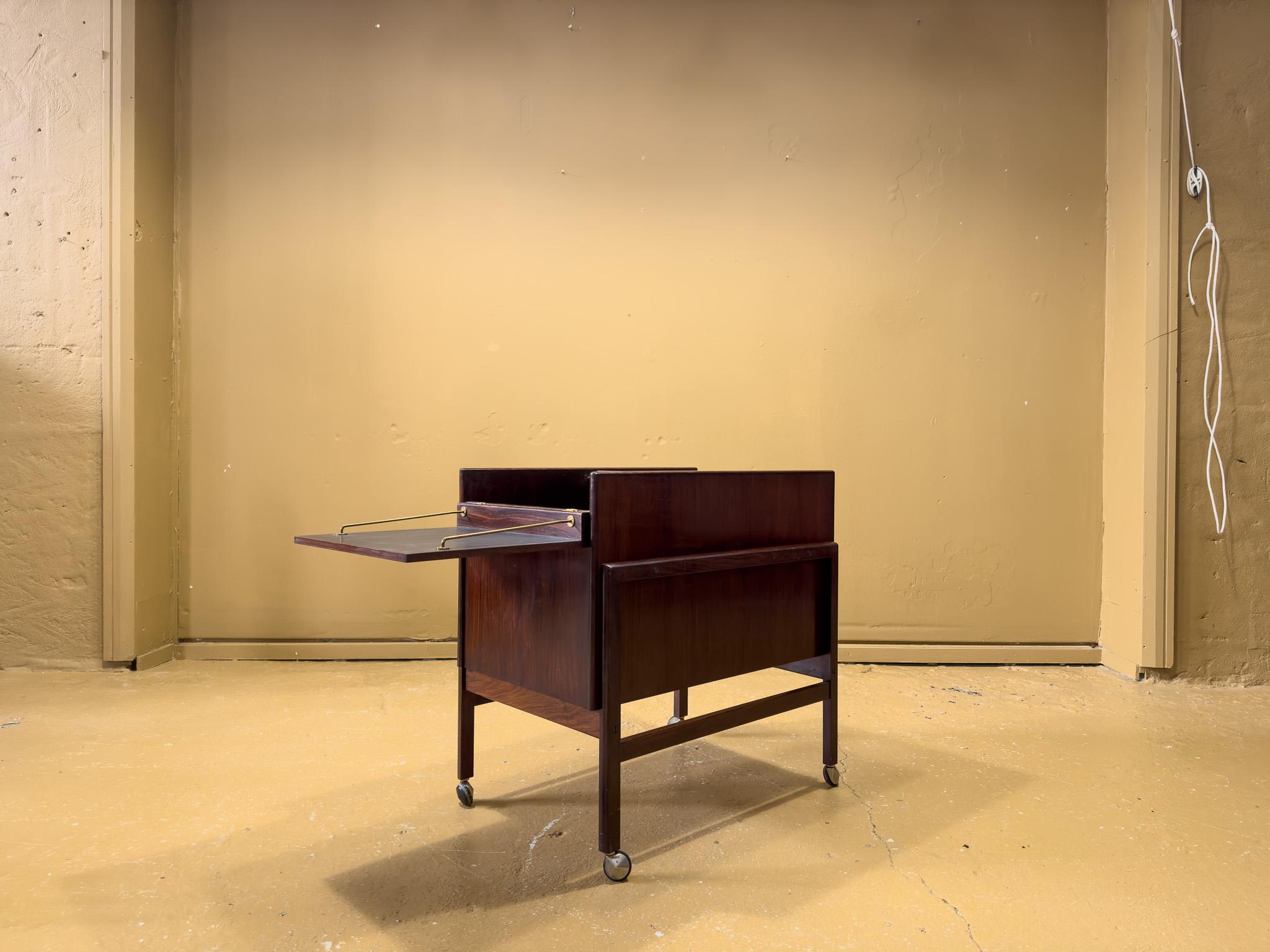 1960s dry bar cart from the Danish manufacturer Dyrlund. The box-like trolley, with its smooth hardwood exterior, brass hardware, chrome castors, and rich navy blue interior lining, is exemplary of the sleek and functional pieces produced by Dyrlund
