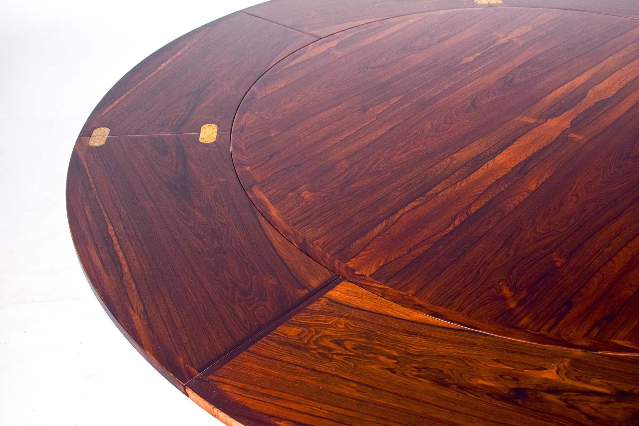 The Dyrlund Flip Flap Lotus Dining Table is a remarkable piece of mid-century modern furniture, designed and crafted in Denmark in the 1960s. This unique dining table features a round rosewood top supported by four tapered legs, embodying the